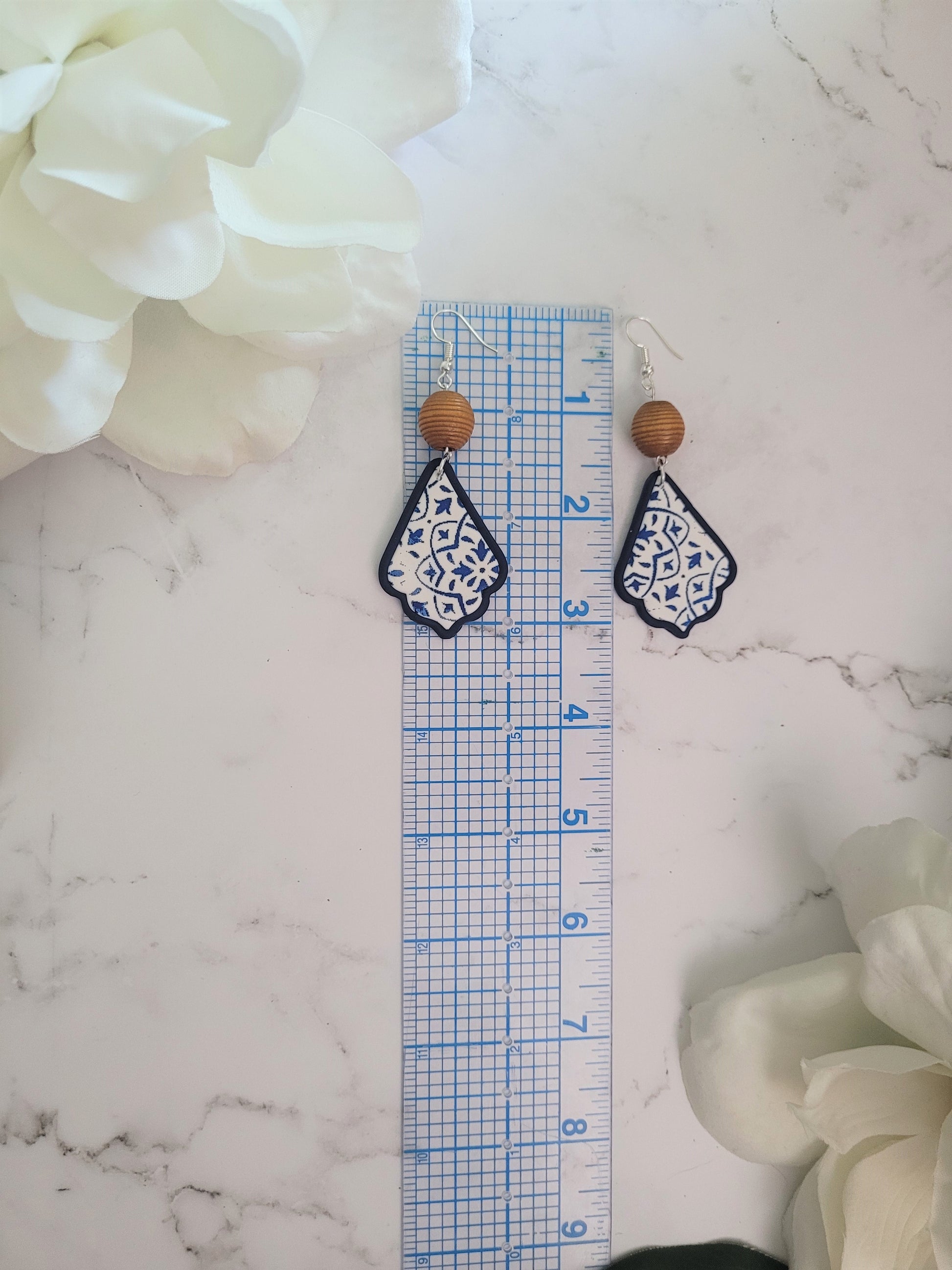 Closeup of Ella style polymer clay earrings on a white background. Earrings are white and navy with a tile print and wood bead.