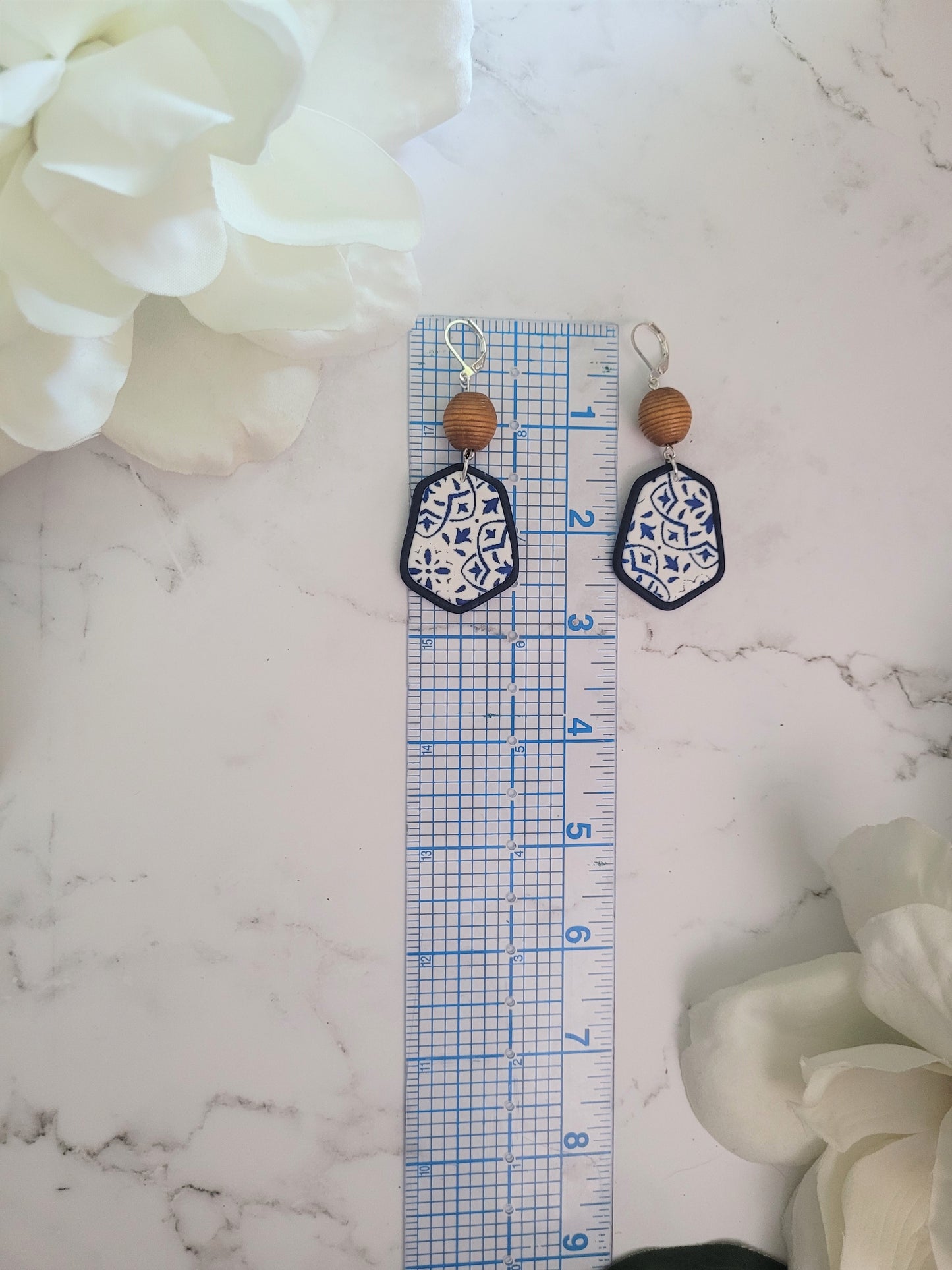 Closeup of Brinn style polymer clay earrings on a white background. Earrings are white and navy with a tile print and wood bead.