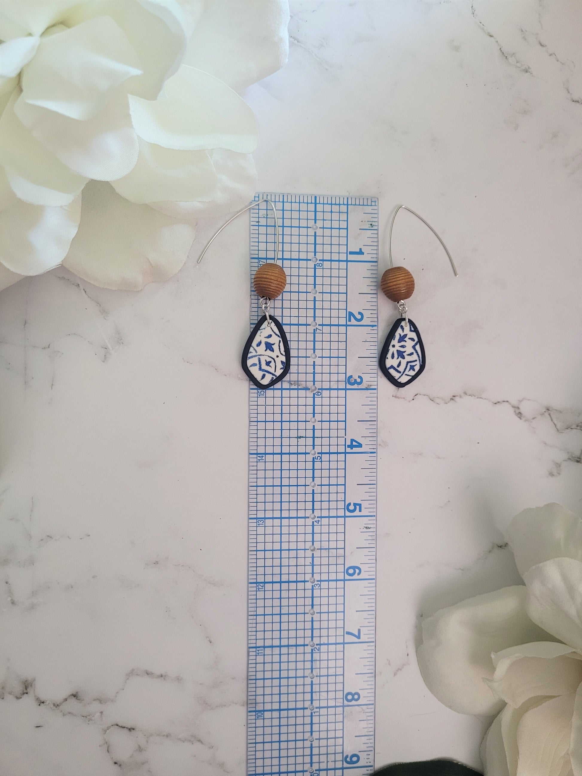 Closeup of Aria style polymer clay earrings on a white background. Earrings are white and navy with a tile print and wood bead.
