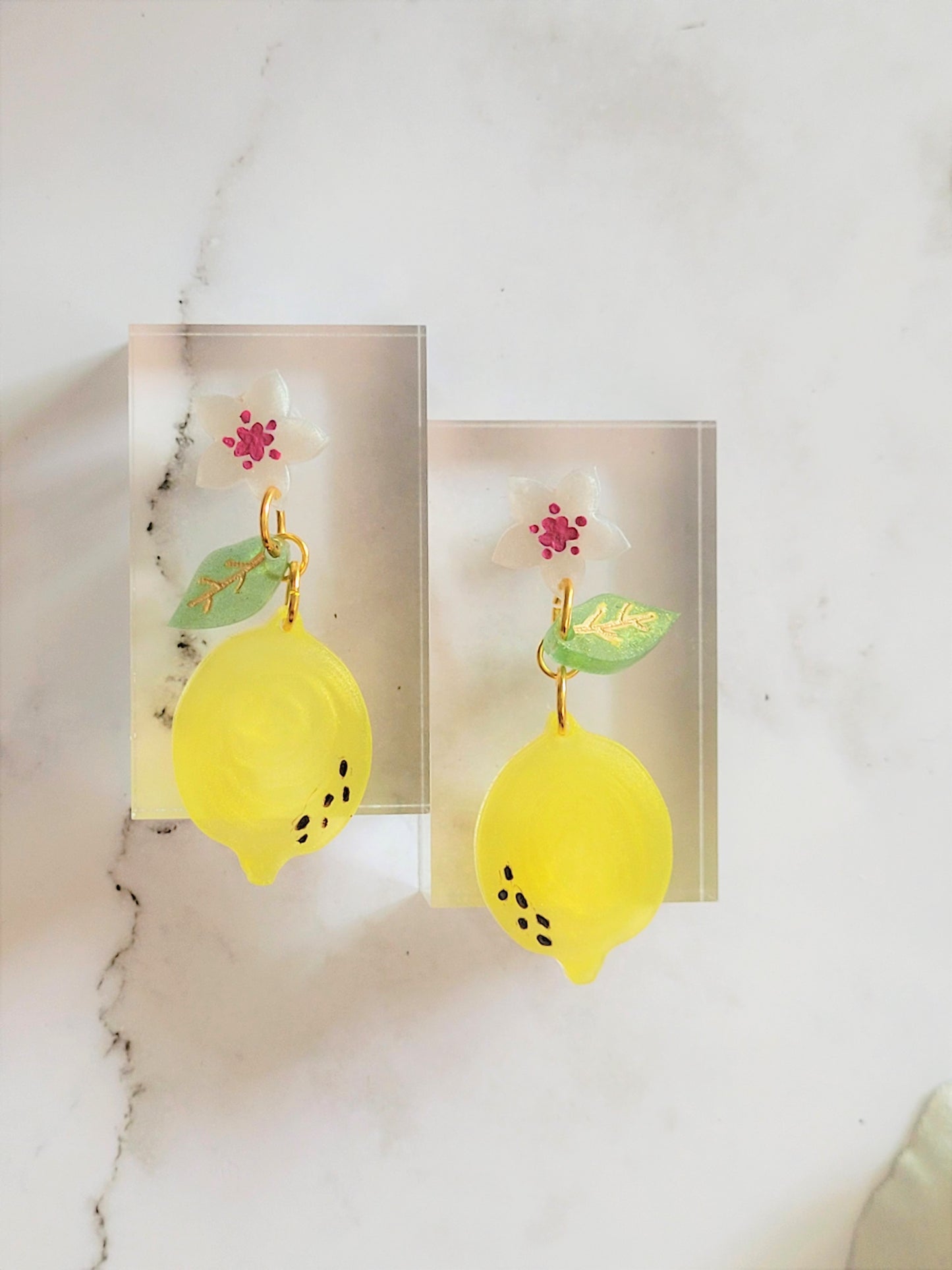 Closeup of resin earring featuring lemon blossom motif (flower, leaf, and fruit).