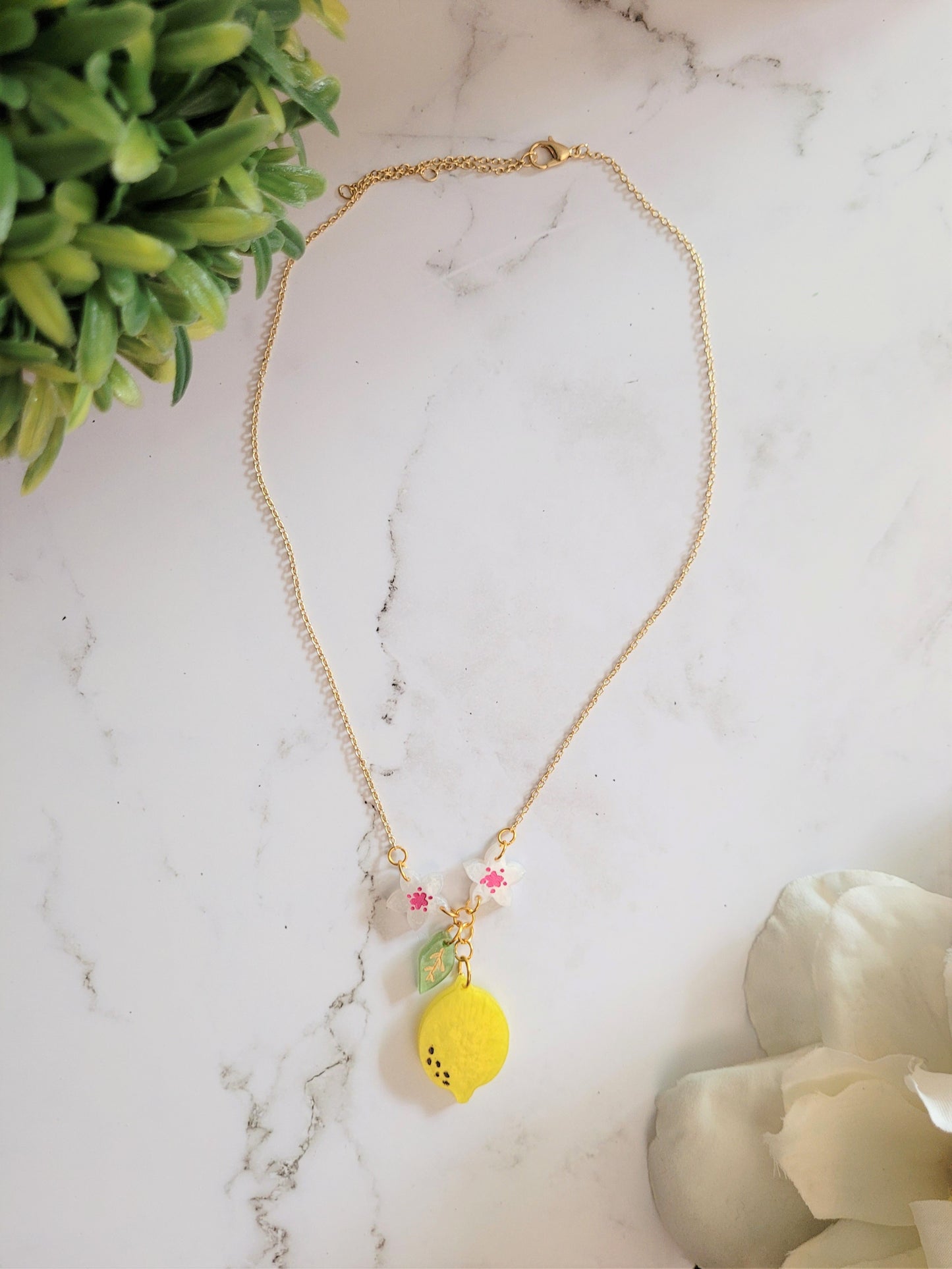 Necklace of lemon blossom, leaf, and fruit dangling from dainty gold chain.