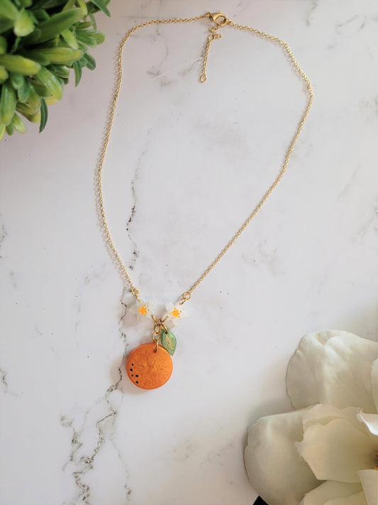 Necklace of orange blossom, leaf, and fruit dangling from dainty gold chain. 