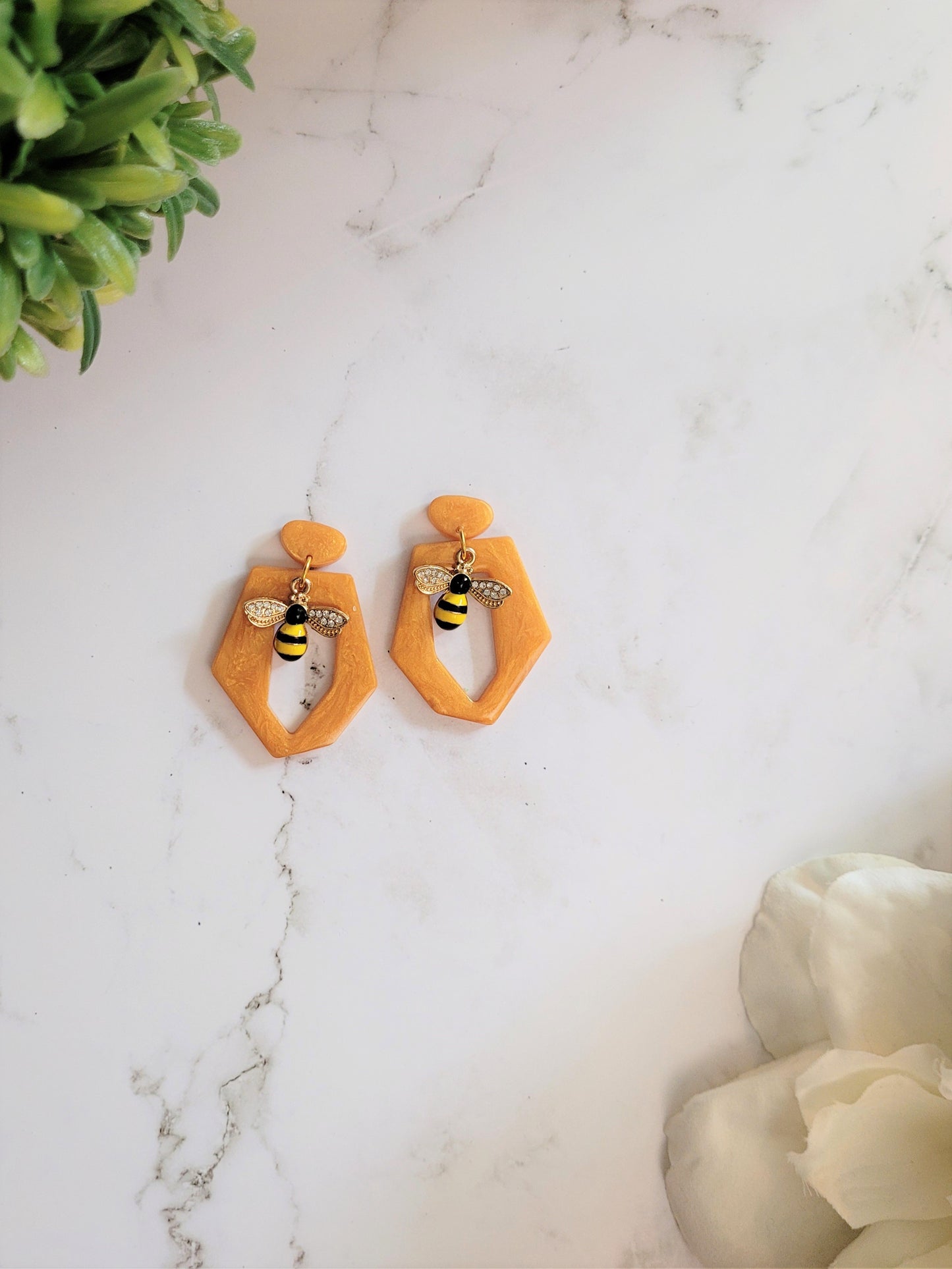 Hexagon shaped resin earring with bee charm on a white background. 