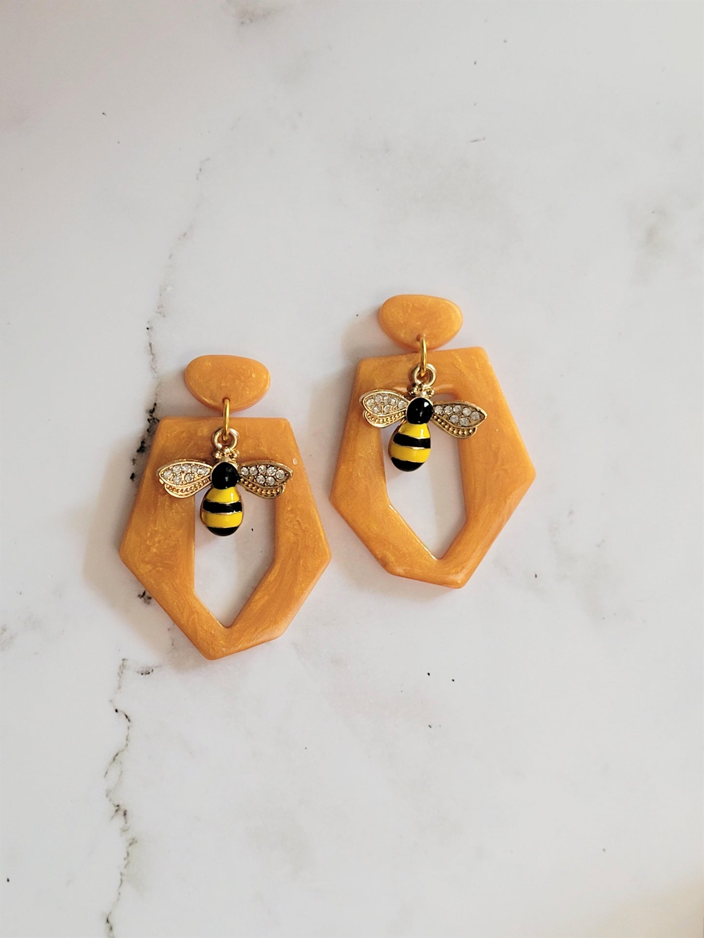 Close up of hexagon shaped resin earring with bee charm on a white background.