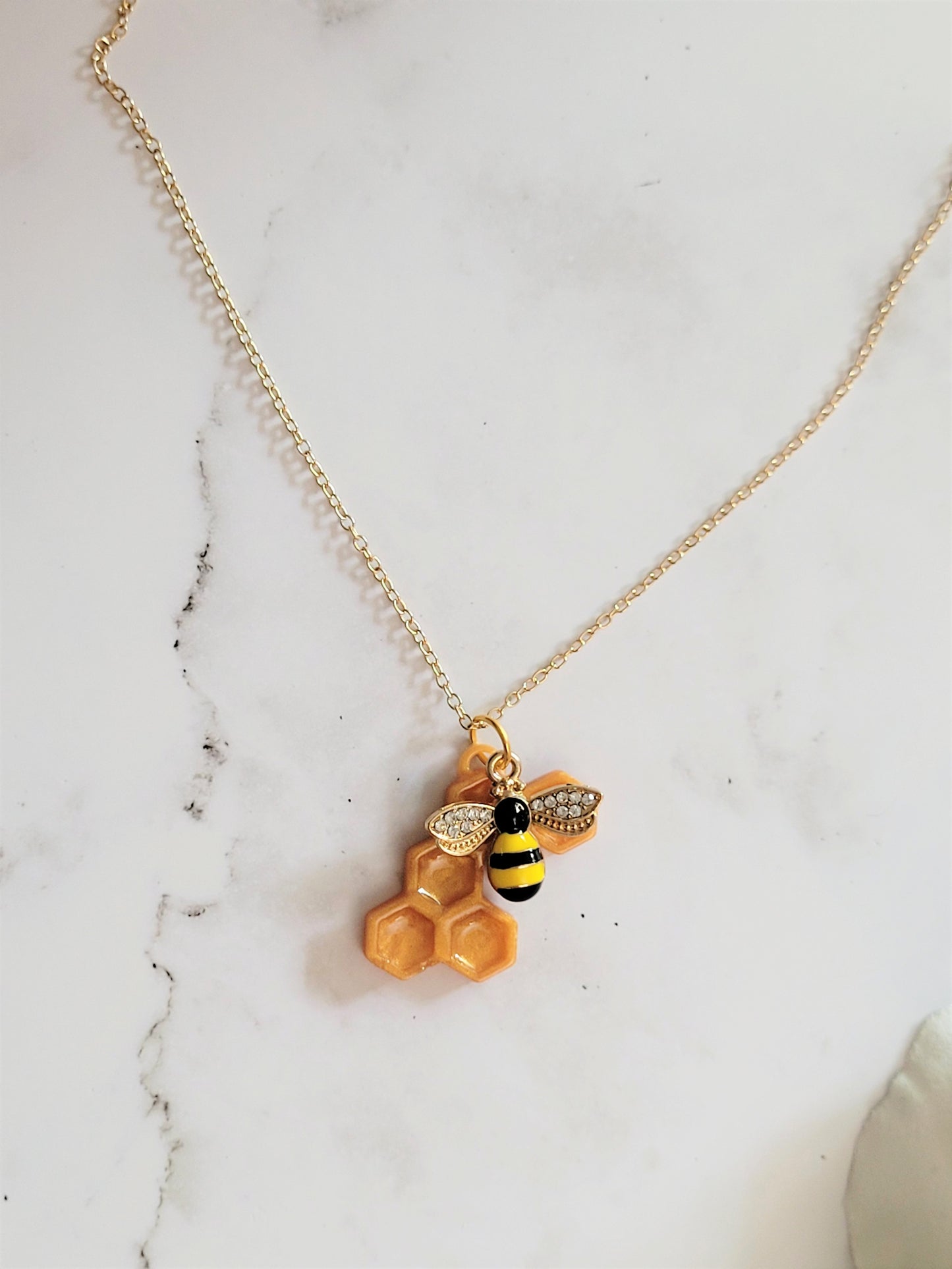 Closeup of honeycomb shaped resin necklace with bee charm on a white background.