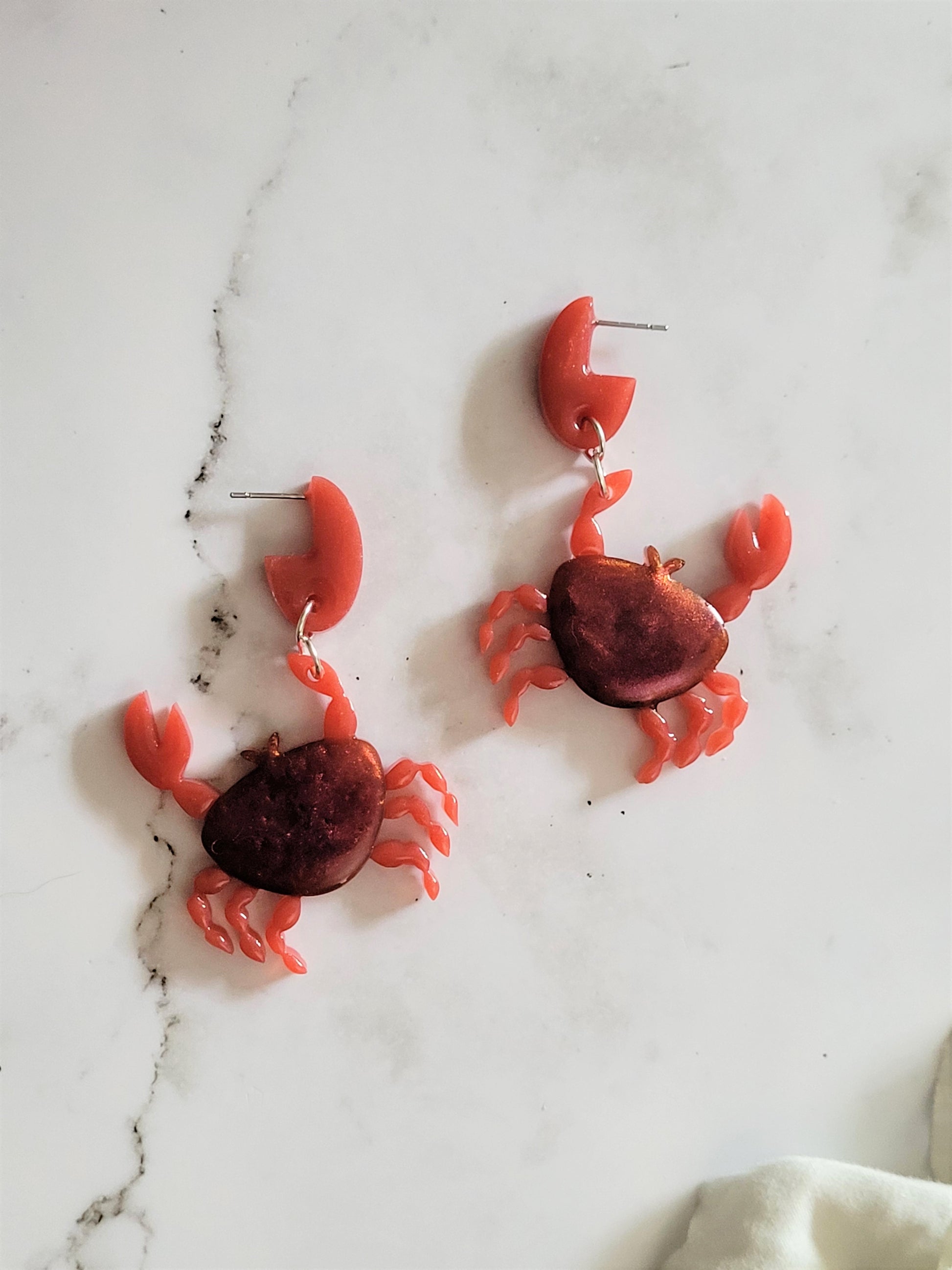 Close up of resin stud earrings in the shape of a red crab with metallic accents. 