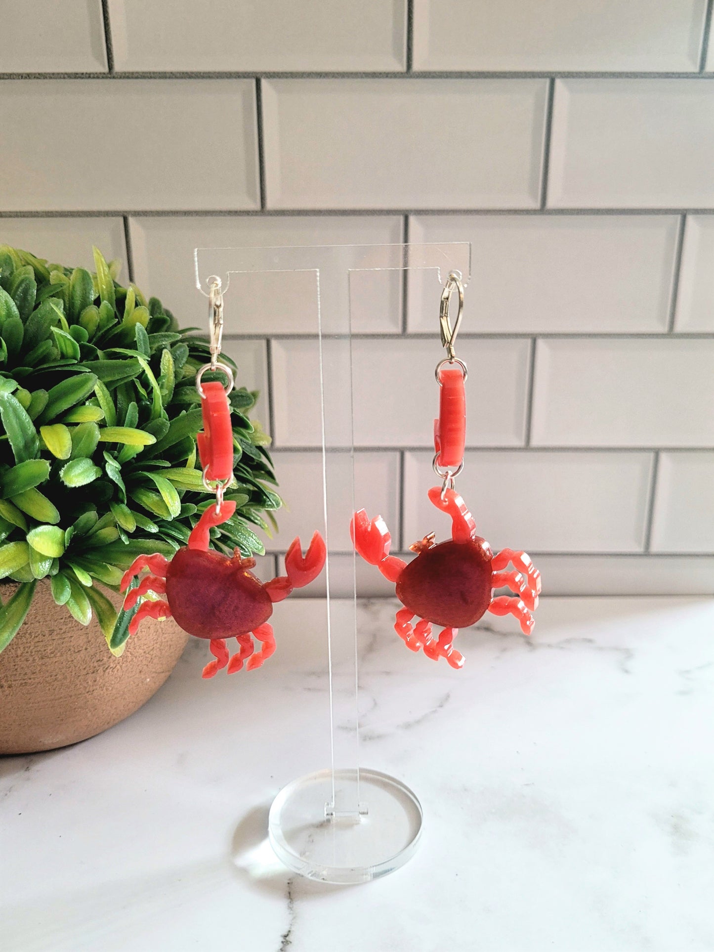 Close up of resin hook earrings in the shape of a red crab with metallic accents on hanger