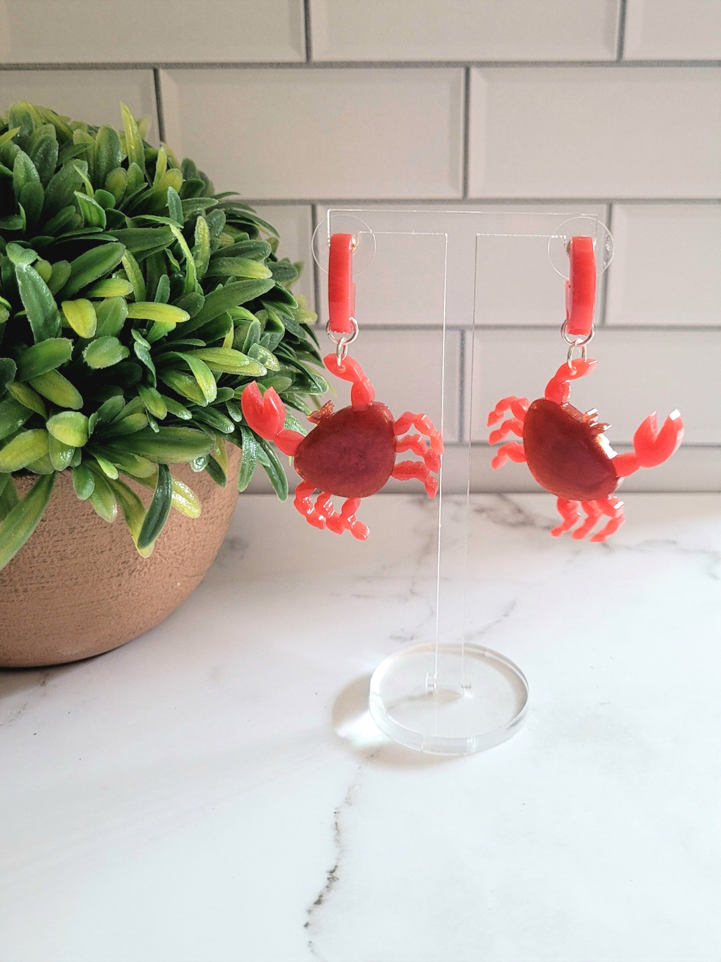 Close up of resin stud earrings in the shape of a red crab with metallic accents on hanger
