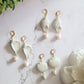 3 Shell shaped polymer clay Earrings on a white background. Earrings are made of pearlescent clay.