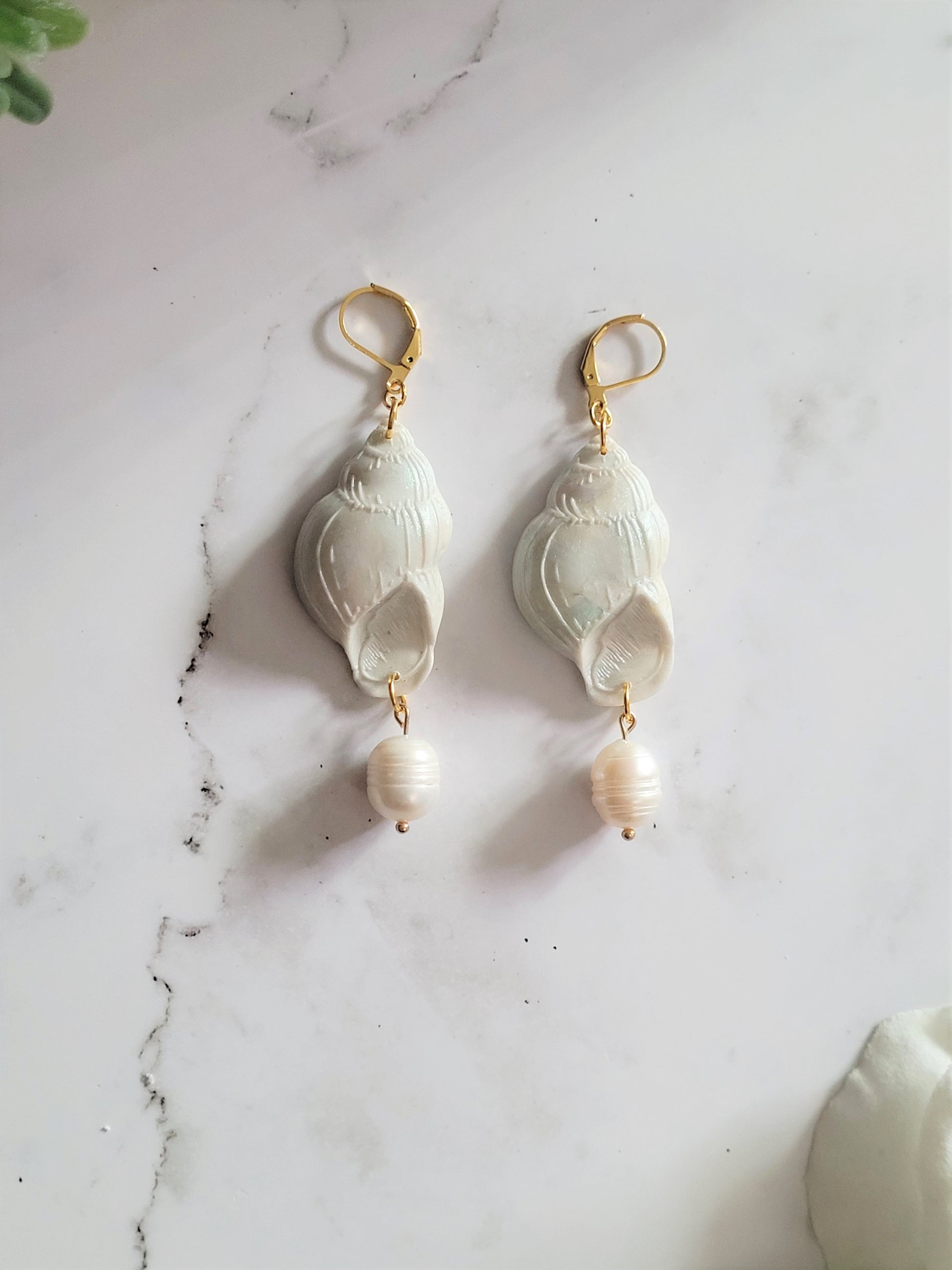 Closeup of periwinkle shell shaped polymer clay Earrings on a white background. Earrings are made of pearlescent clay.
