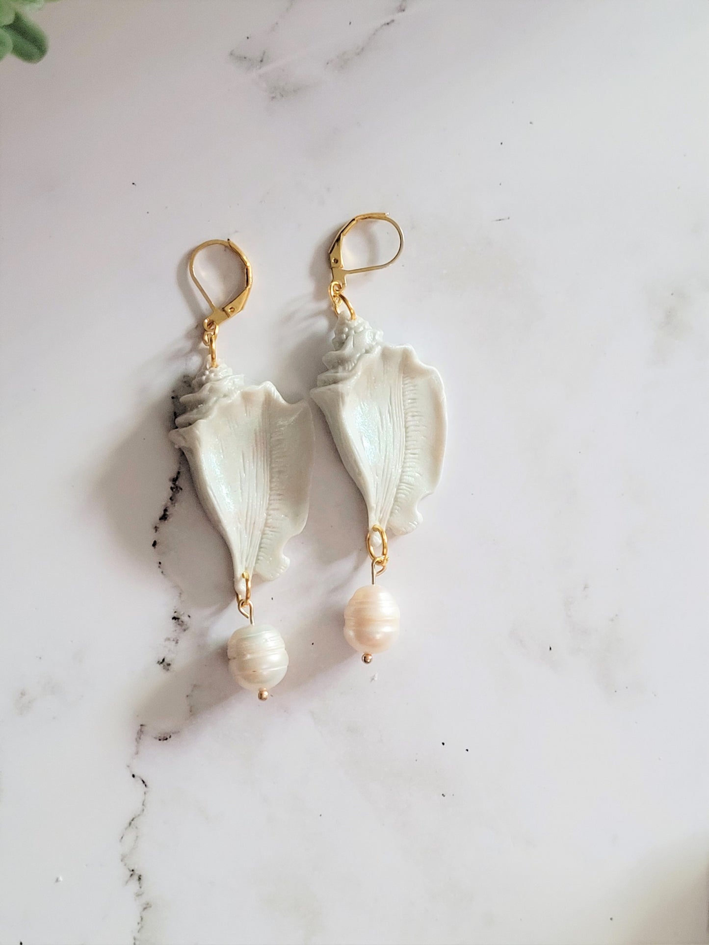 Closeup of conch shell shaped polymer clay Earrings on a white background. Earrings are made of pearlescent clay.