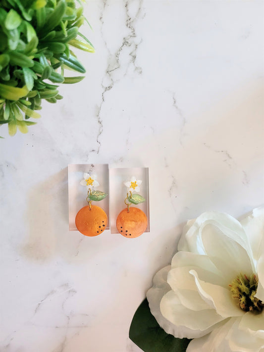 Resin earrings of orange blossom, with fruit and leaf dangling below. 