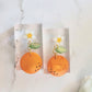 Closeup of resin earring featuring orange blossom motif (flower, leaf, and fruit). 