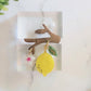 Resin brooch of tree branch with a flower, lemon, and leaf dangling from it.