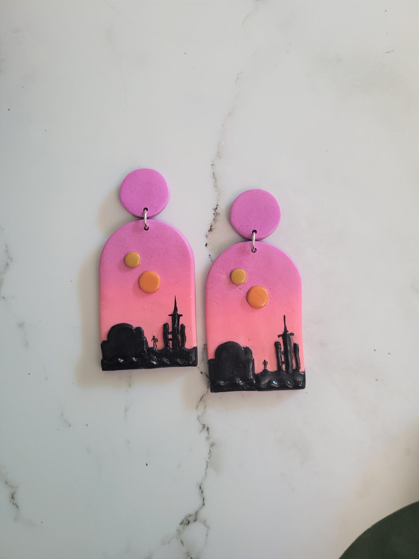 Closeup of Arch earrings with a sunset landscape