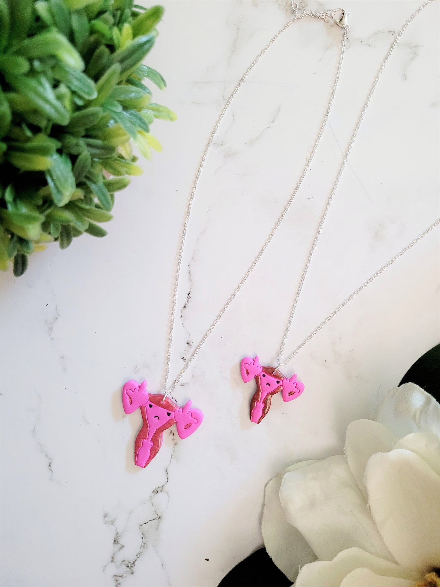 Pink uterus necklace with middle finger fallopian tubes. 
