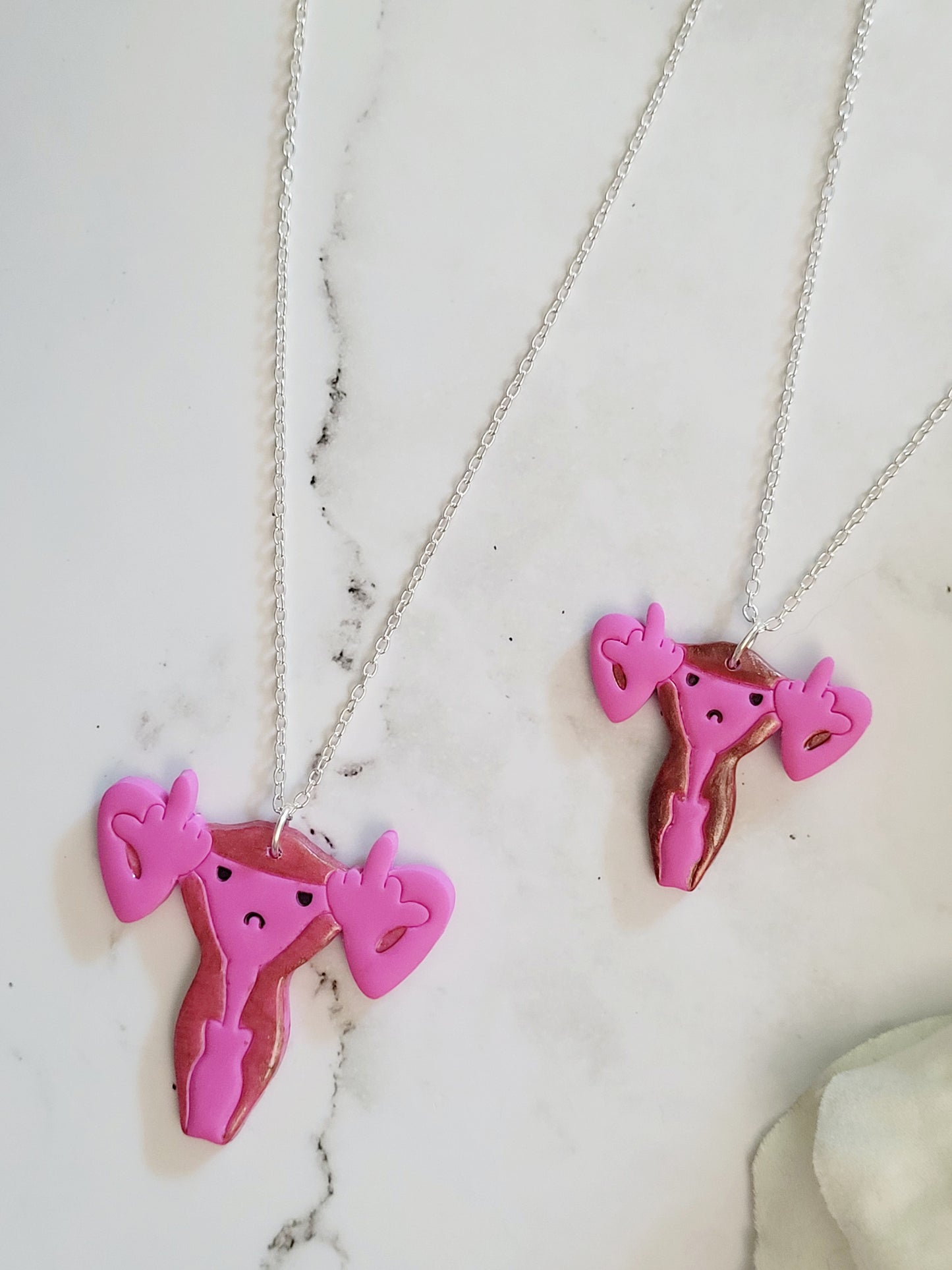 closeup of Pink uterus necklace with middle finger fallopian tubes. 