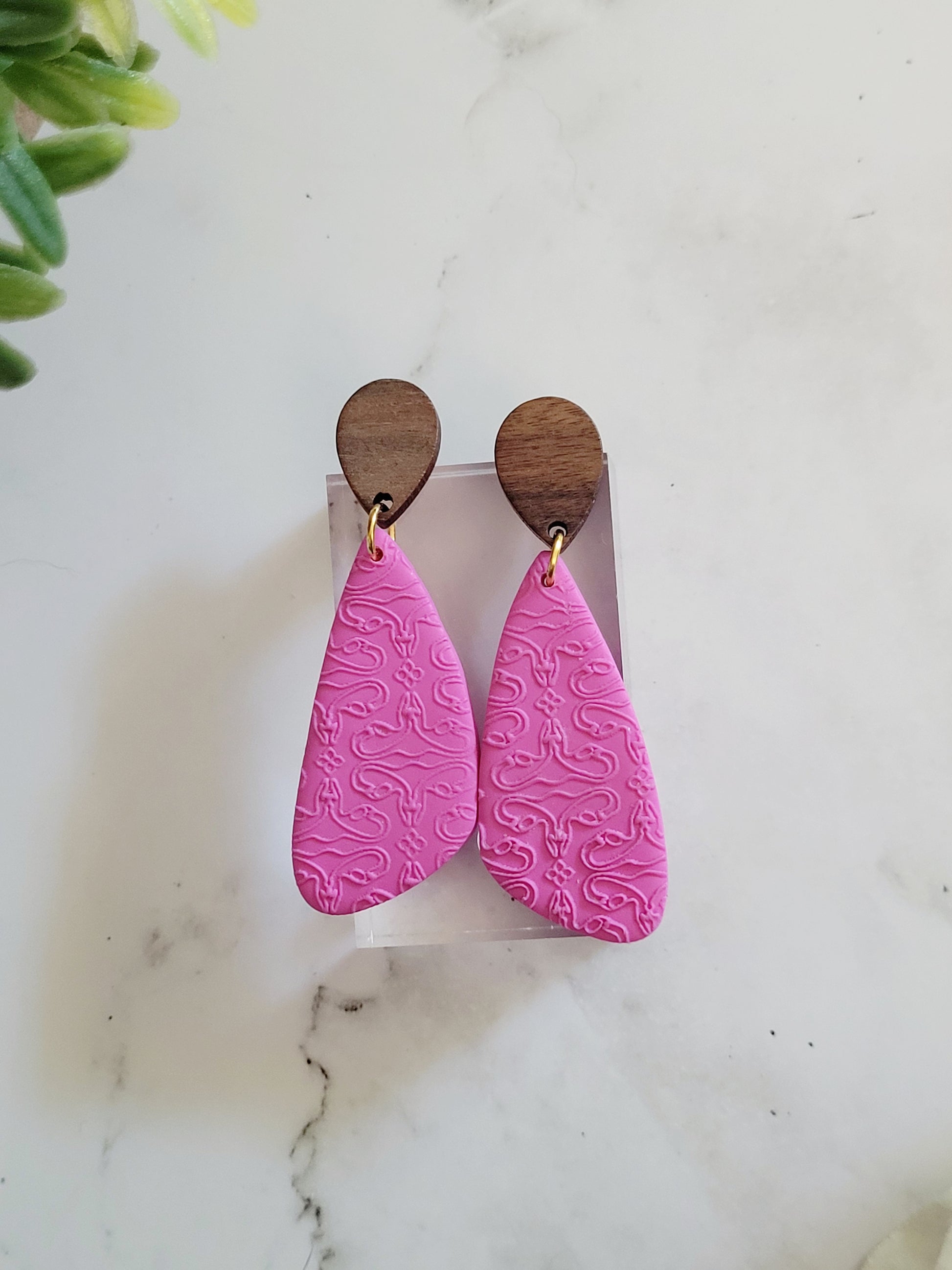 close up of pink wood and clay earrings with uterus embossing.