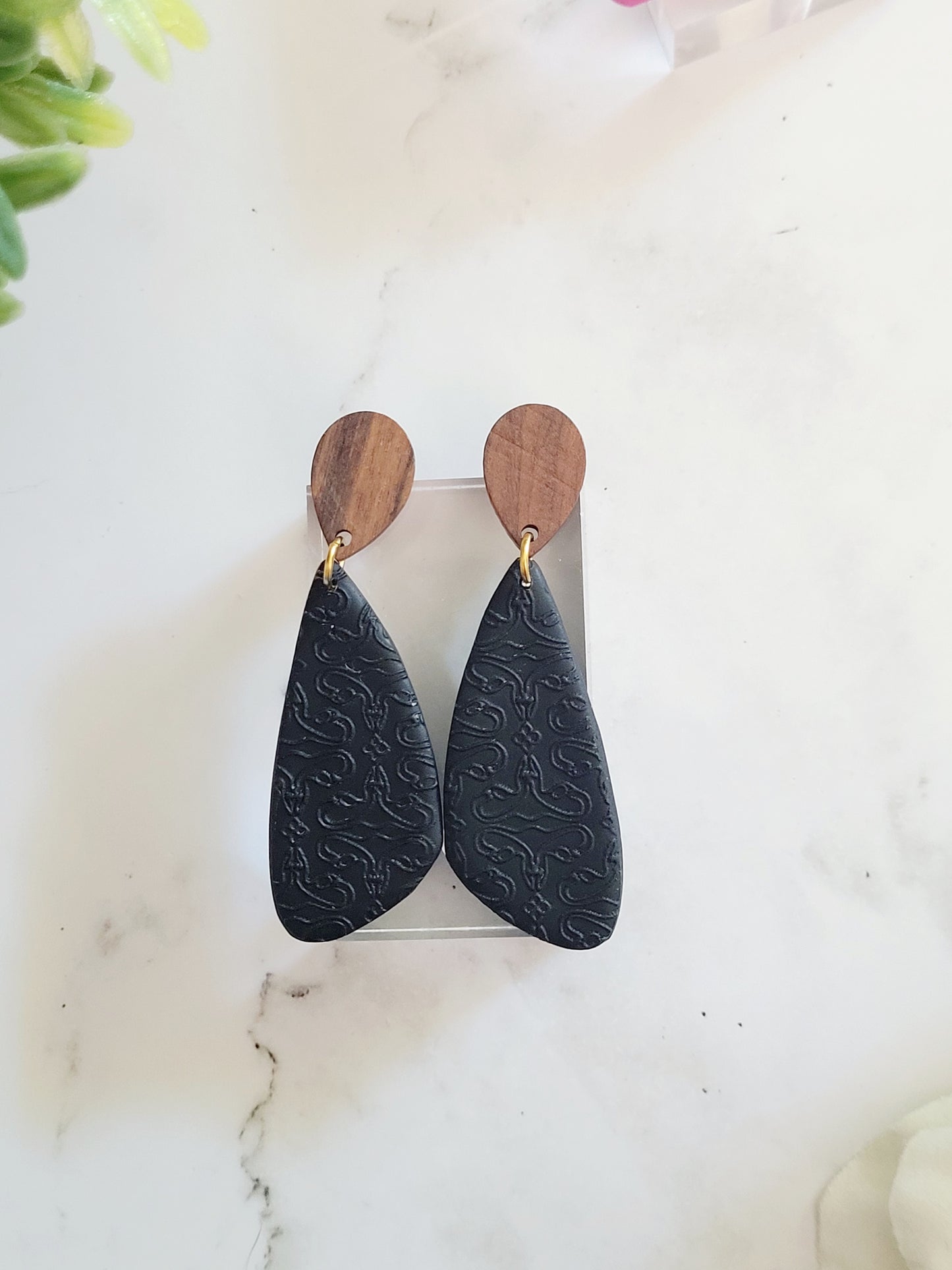 close up of black wood and clay earrings with uterus embossing.