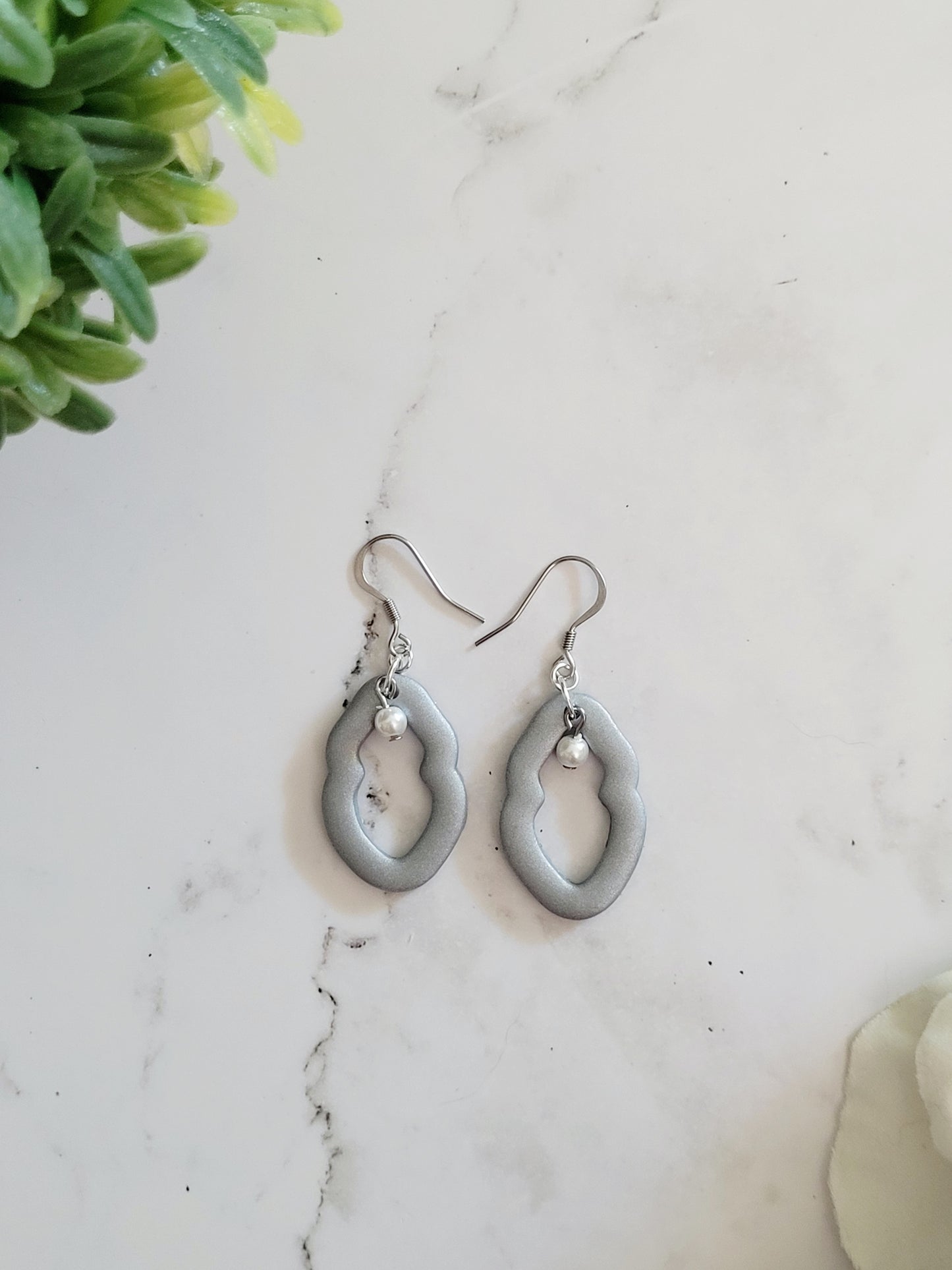 Closeup of small silver Vulva shaped earrings with pearl bead