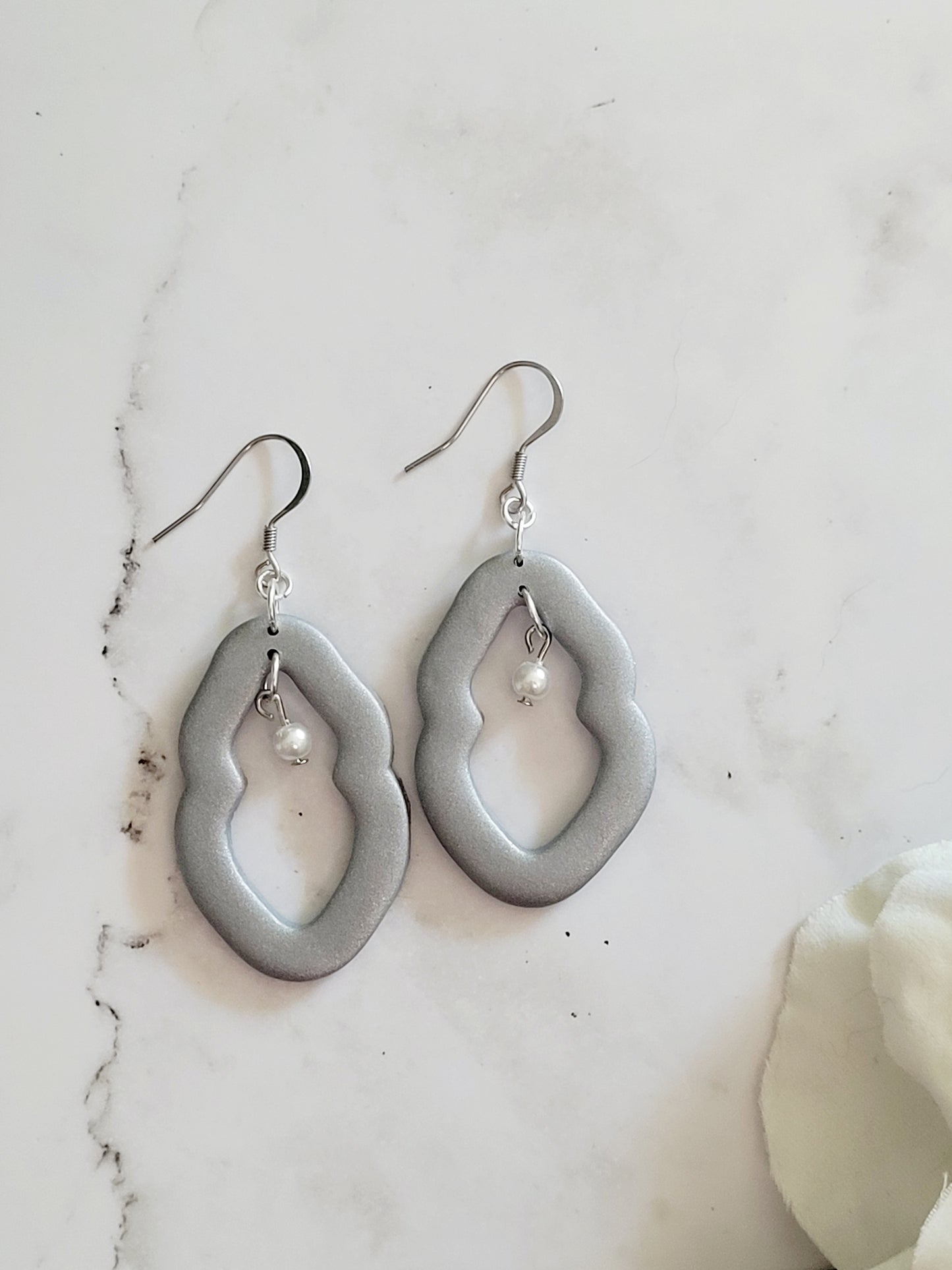 Closeup of large silver Vulva shaped earrings with pearl bead