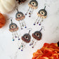 All seeing eye earrings in three skin tones on a white marble background with pumpkins and flowers. 