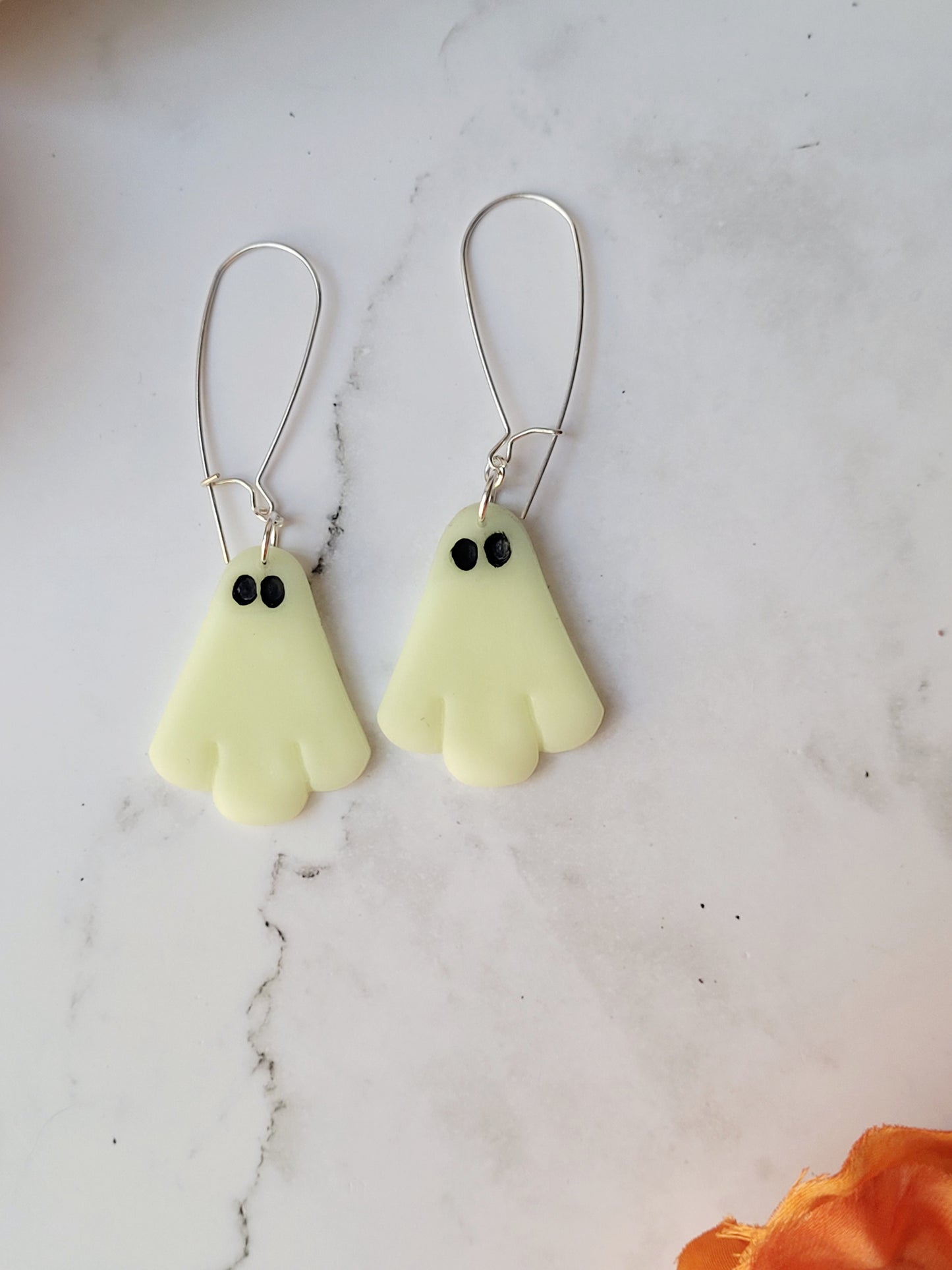 close up of glow in the dark ghost earrings on a white marble background.