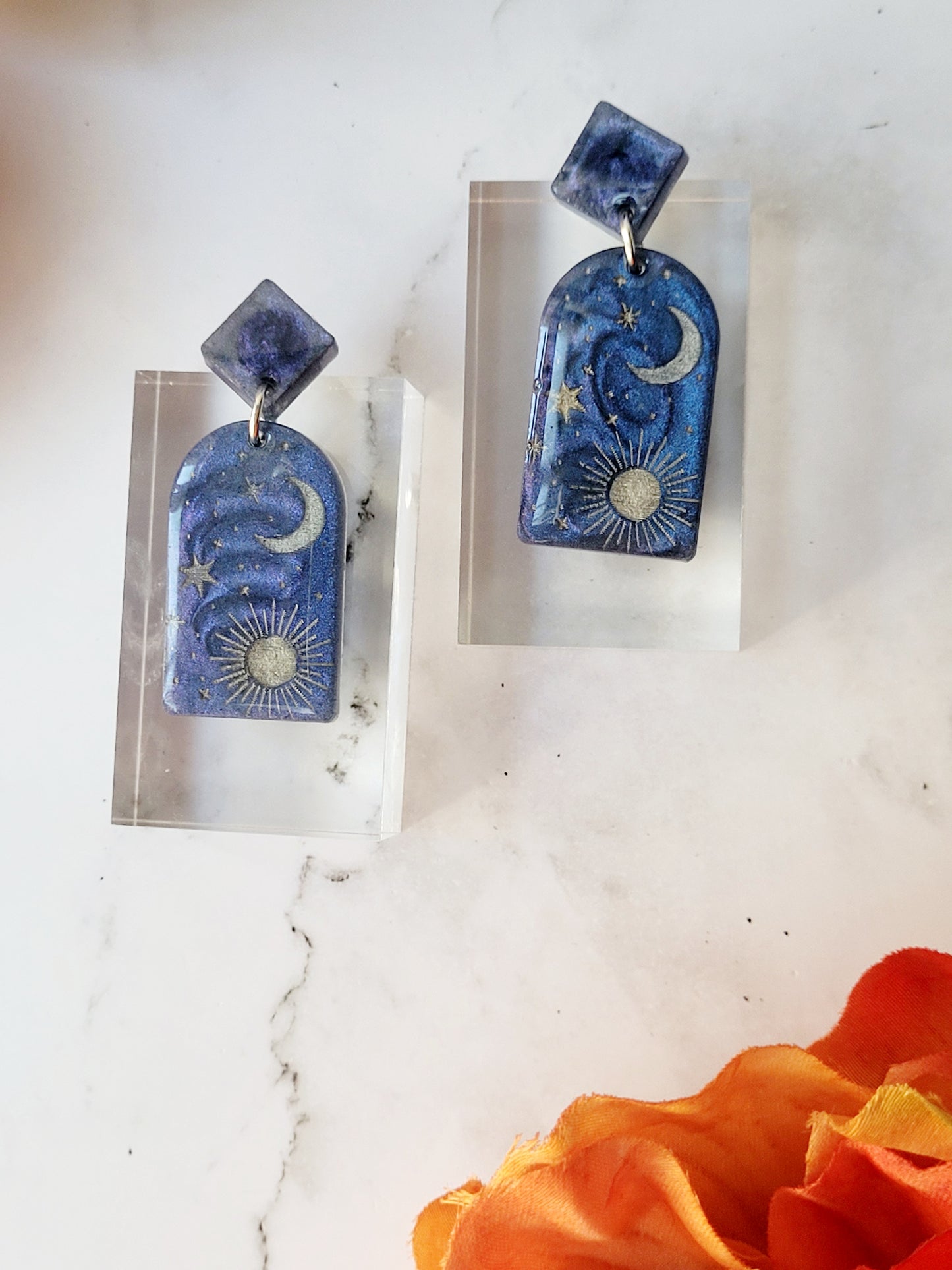 close up of blue arch earrings with painted celestial details on a marble background.