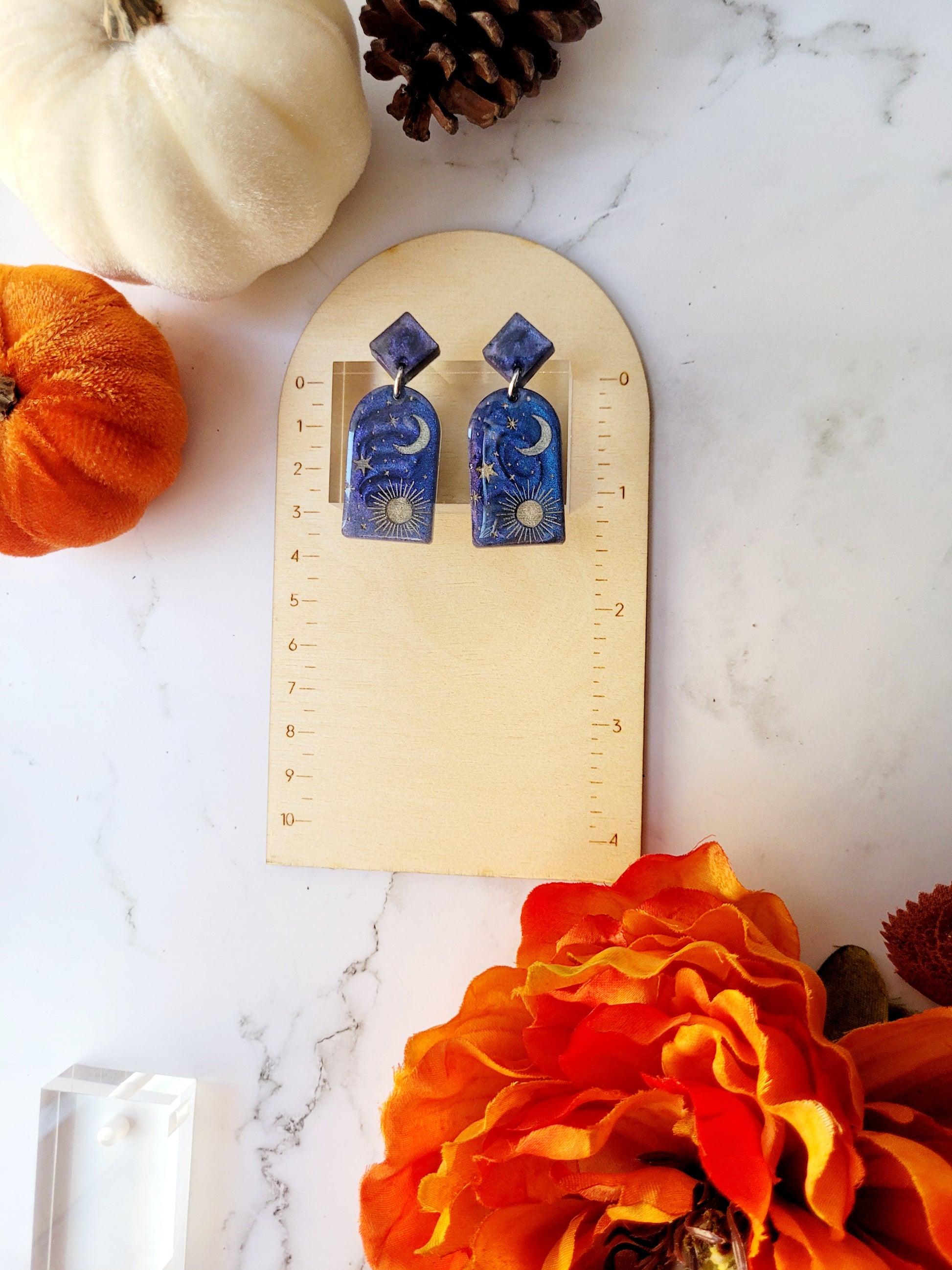 blue arch earrings with painted celestial details on a ruler background.