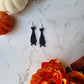 Black Hanging bat earrings on a white marble background .