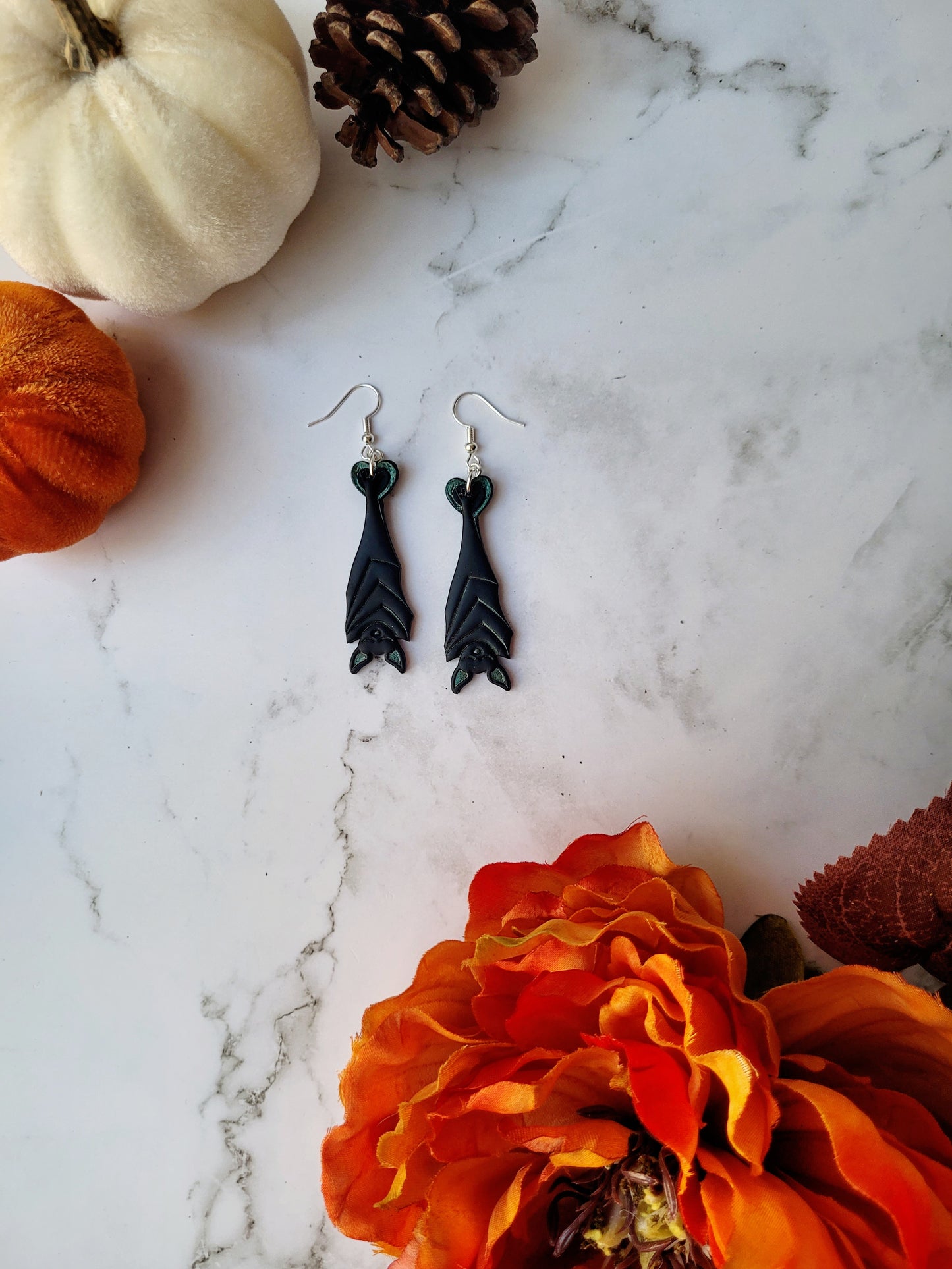 Black Hanging bat earrings on a white marble background .