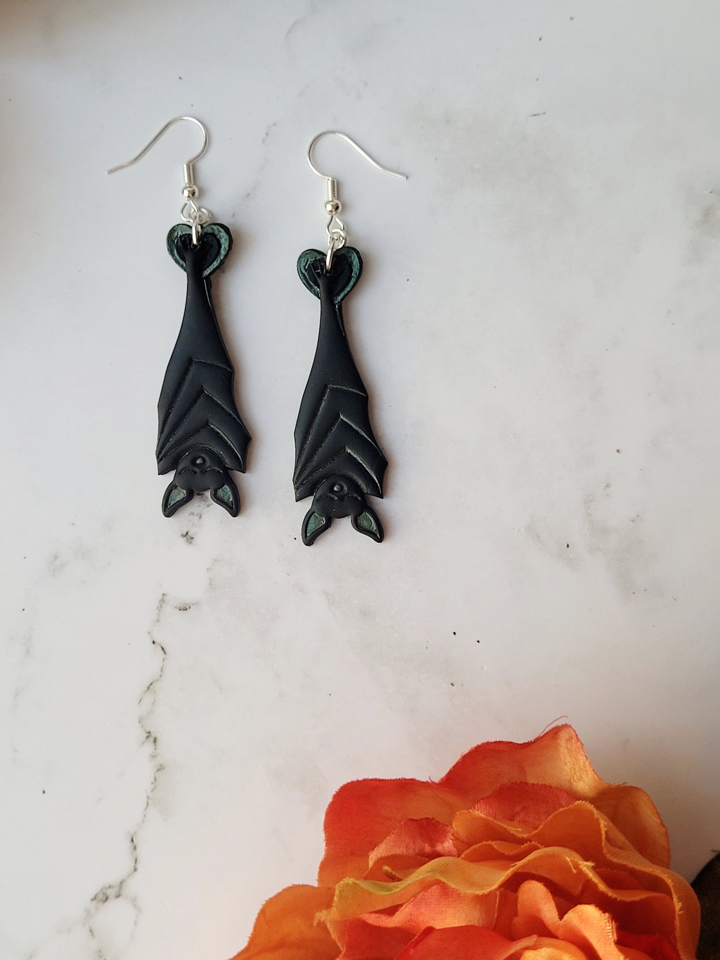 close up of Black Hanging bat earrings on a white marble background .
