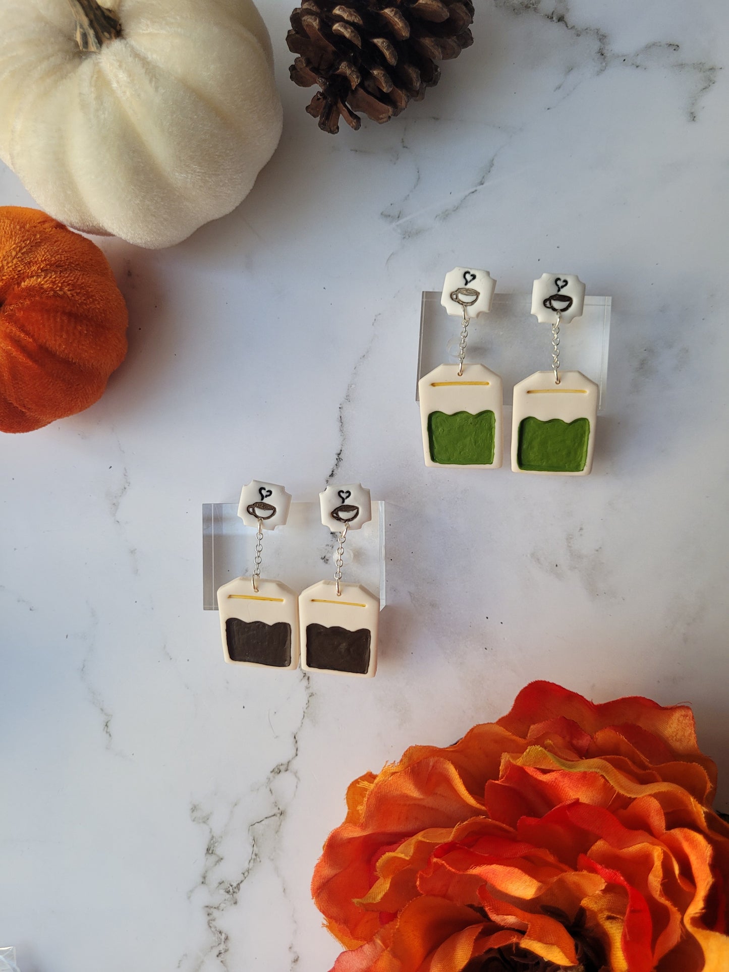 green and black tea bag shaped dangle earrings on a marble background with fall foliage. 