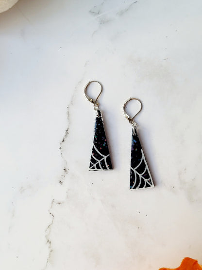 close up of triangular black glitter earrings with white spider webs
