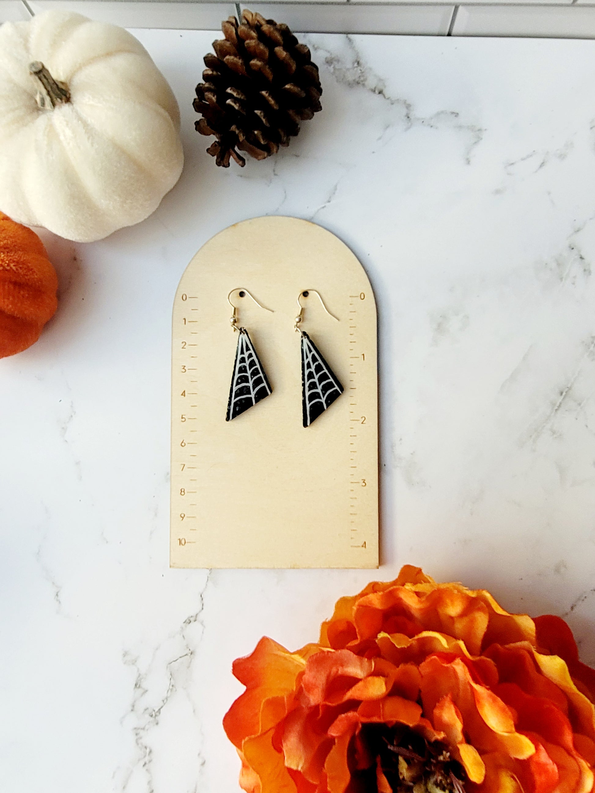 close up of asymmetrical black glitter earrings with white spider webs on ruler