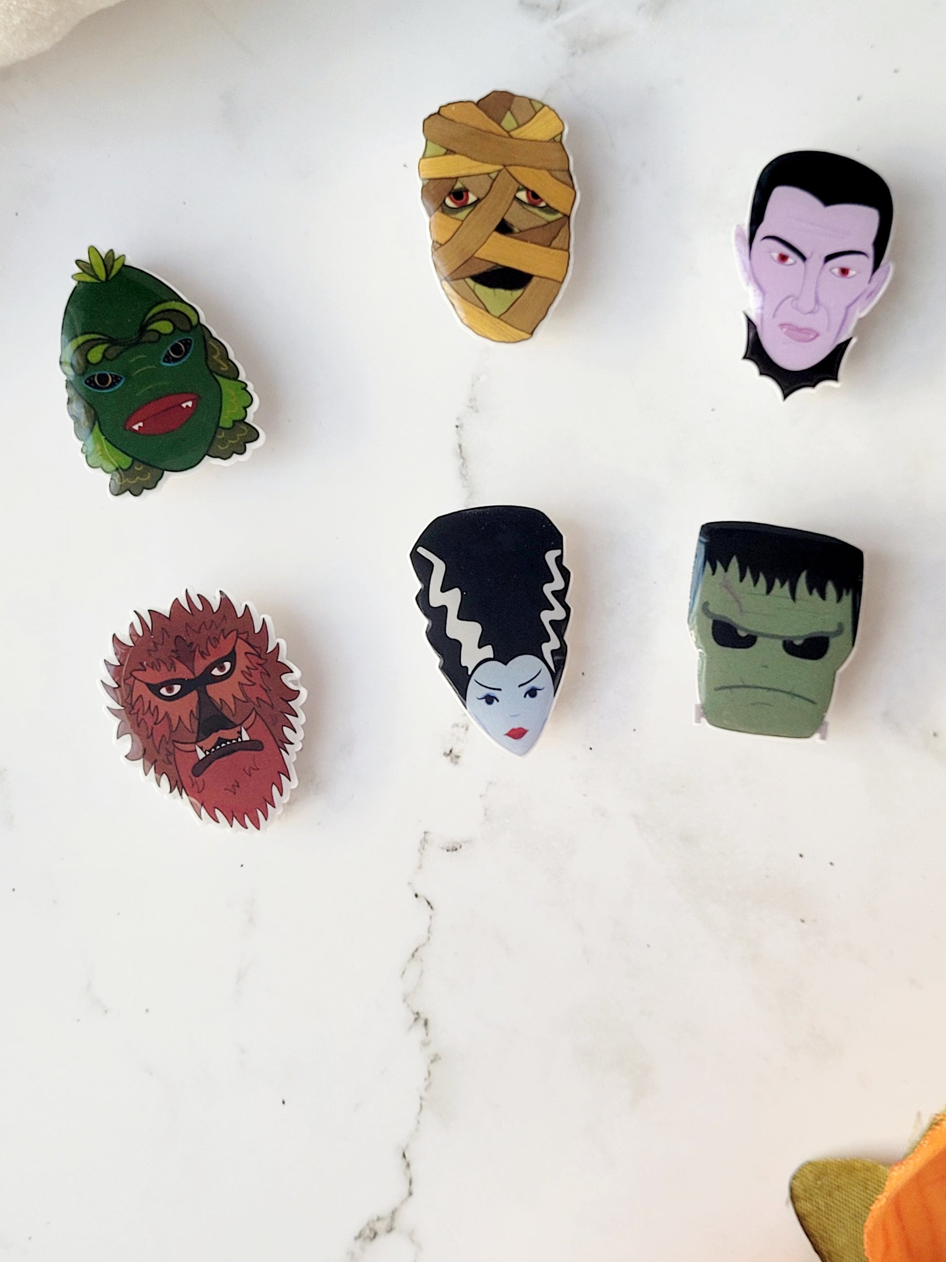 close up of 6 universal monster head lapel pins on a marble background
