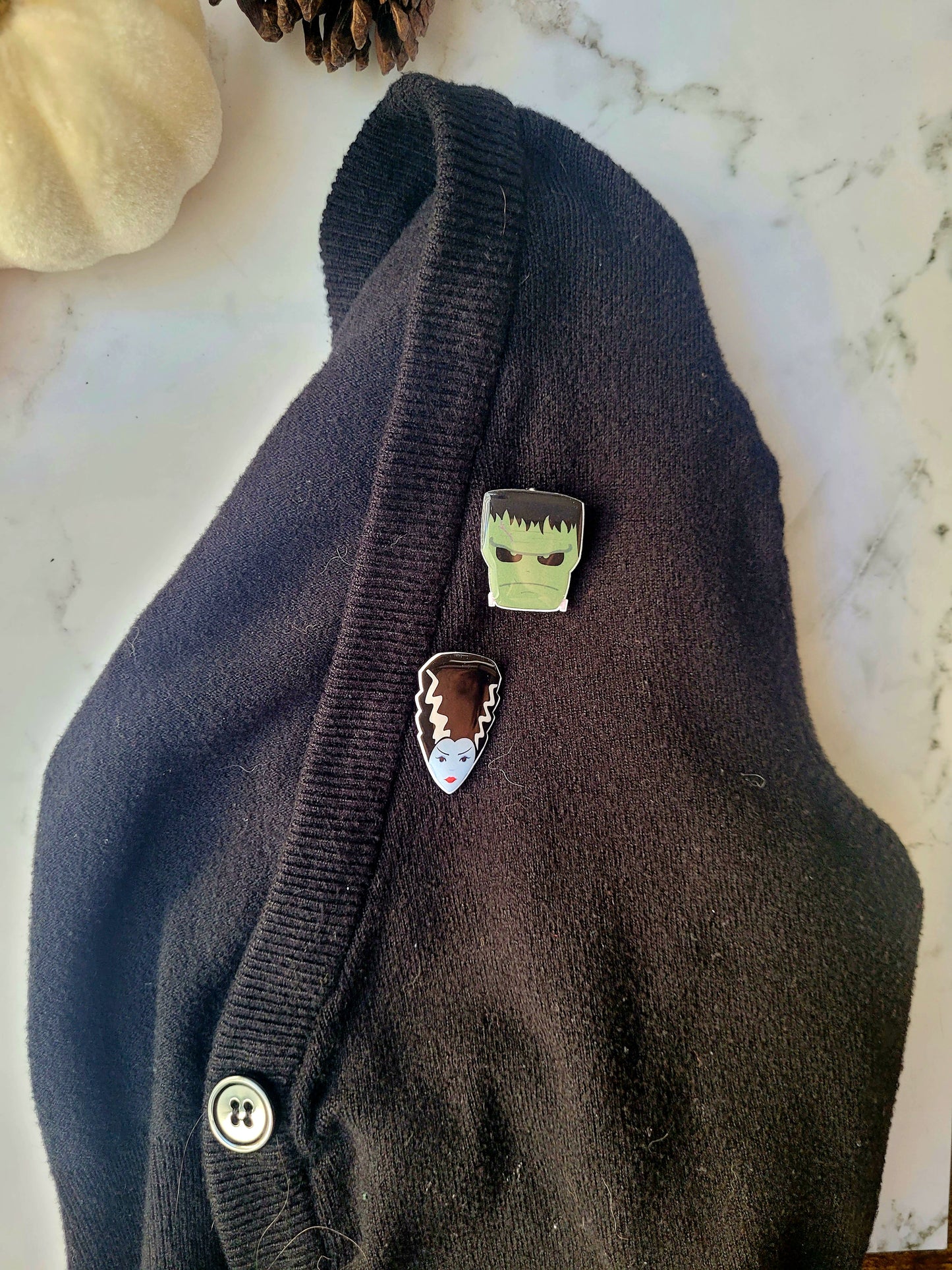 Frankenstein and Bride of Frankenstein monster pins on a black cardigan. 