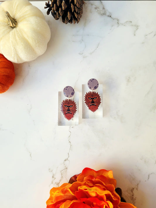 Wolfman head dangle earring with moon stud on a marble background with fall foliage. 