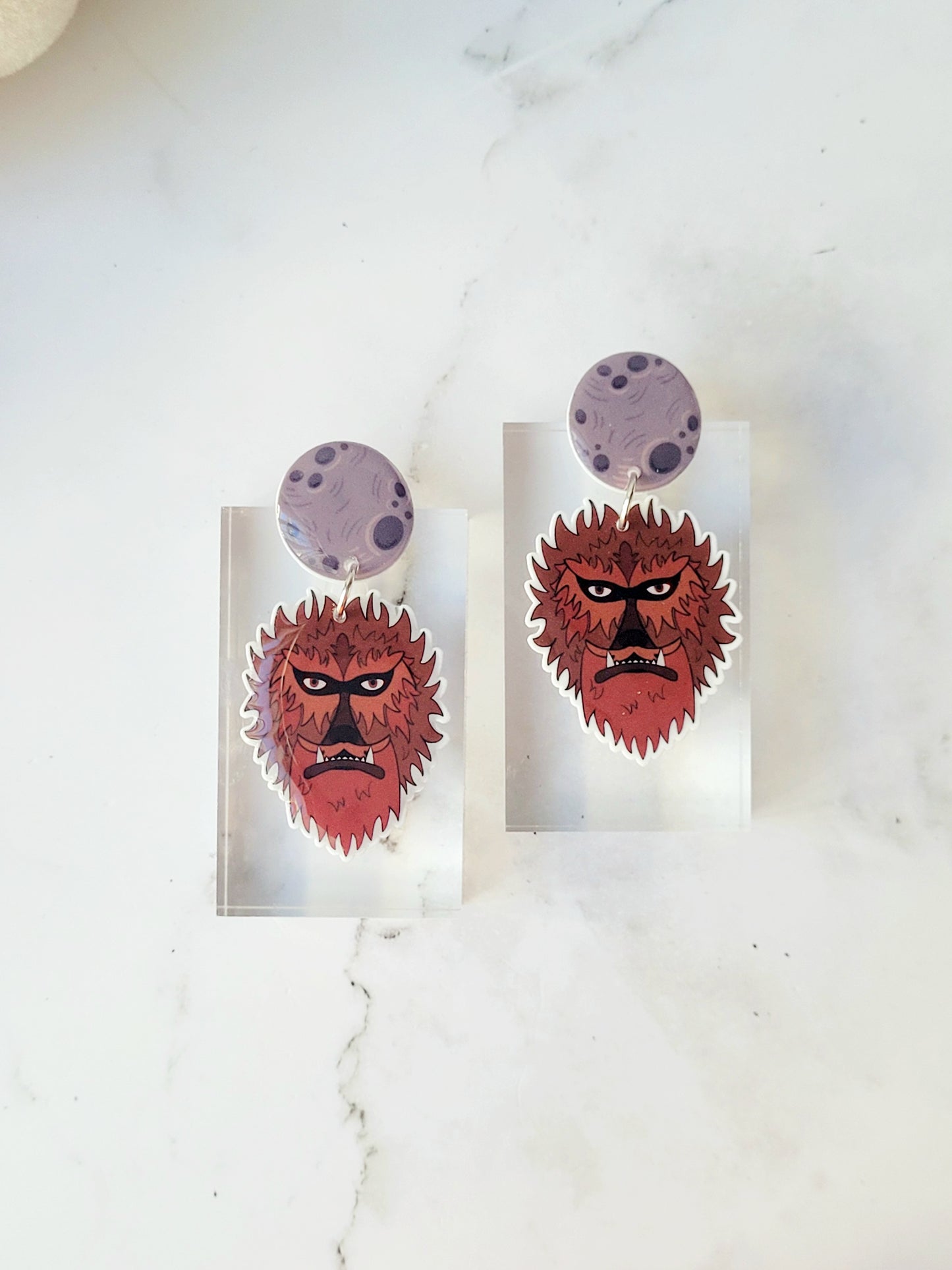 close up of Wolfman head dangle earring with moon stud on a marble background 