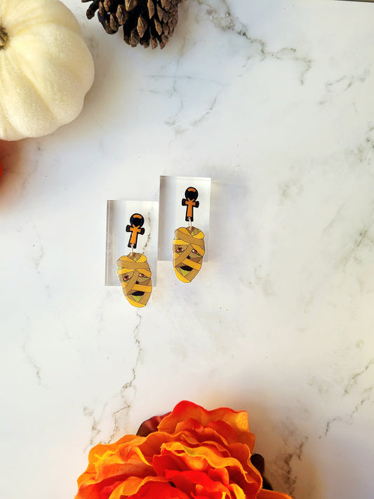 mummy head dangle earrings with ankh stud on a marble background with fall foliage. 