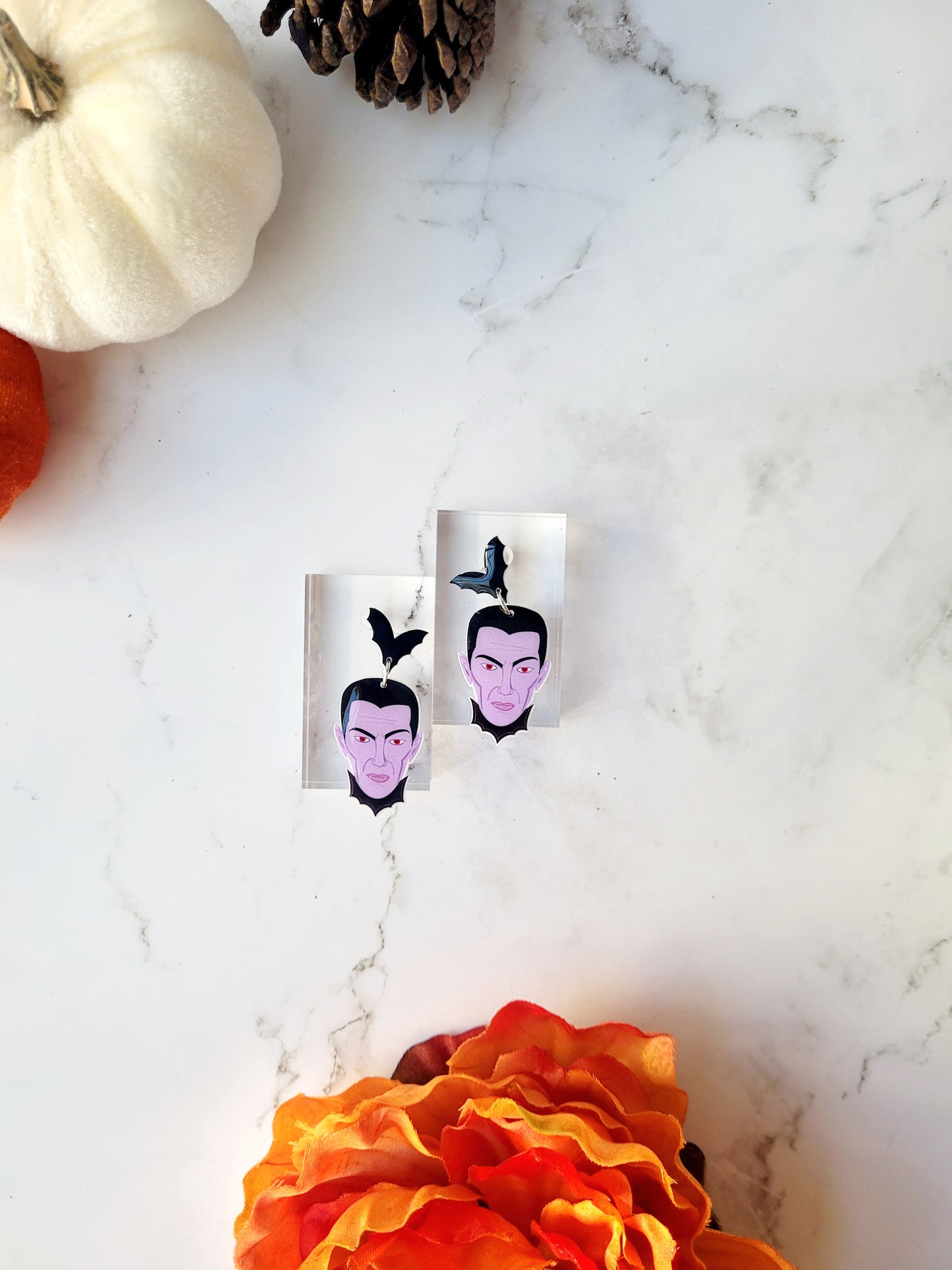dracula dangle earrings on a white marble background with fall foliage. 