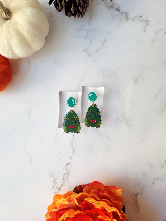 creature of the black lagoon earrings on a marble background surrounded by foliage. 