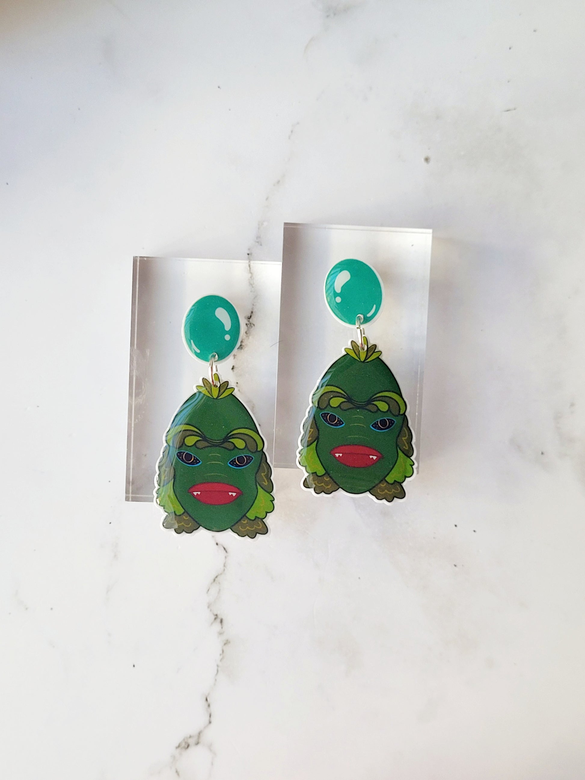 close up of creature of the black lagoon earrings on a marble background.