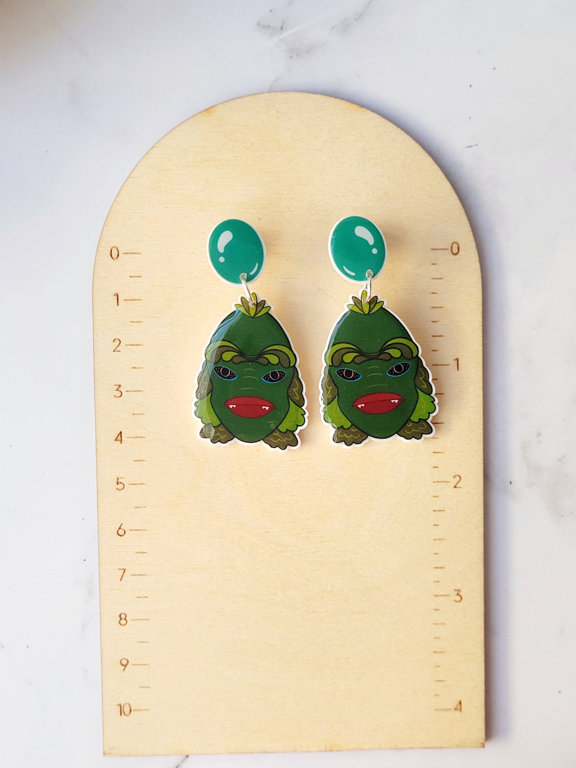 close up of creature of the black lagoon earrings on a ruler background.