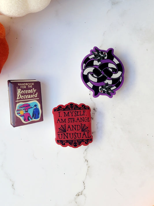 close up of 3 Beetlejuice themed brooches on a white marble background 