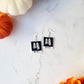Beetlejuice inspired "no feet" ghost polaroid earrings on a marble background with fall foliage. 