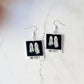 close up of Beetlejuice inspired "no feet" ghost polaroid earrings on a marble background