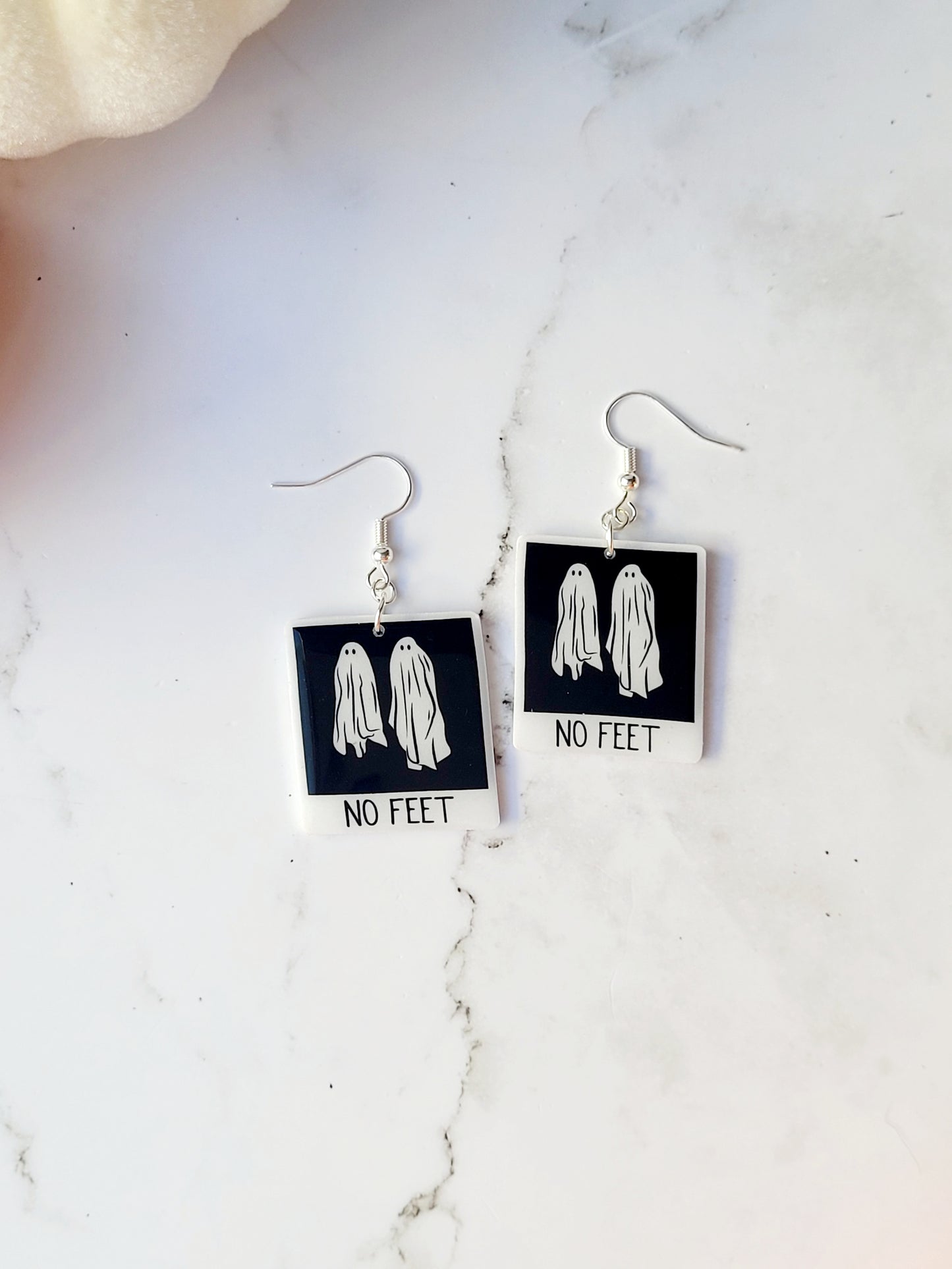 close up of Beetlejuice inspired "no feet" ghost polaroid earrings on a marble background