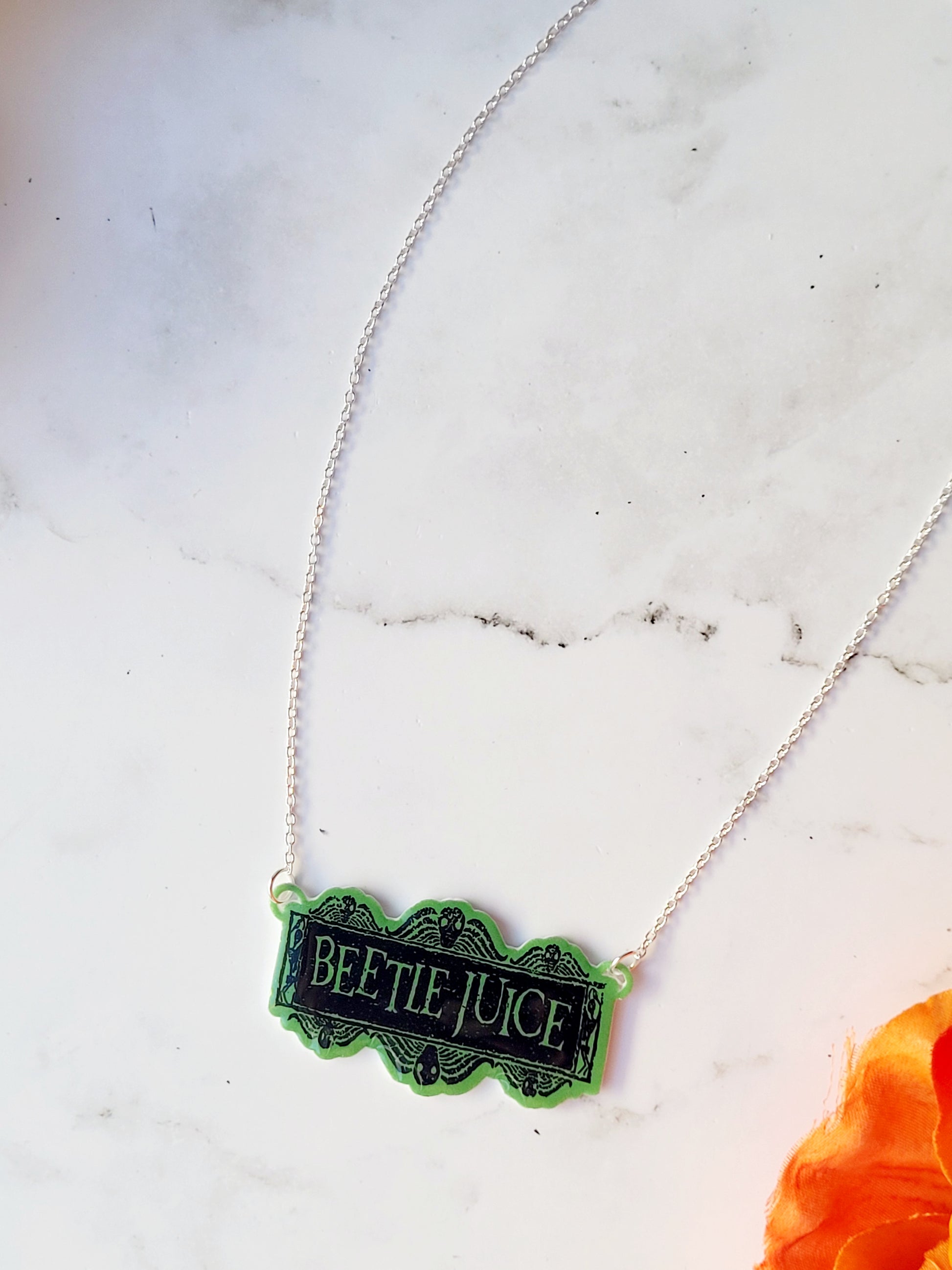 Close up of Beetlejuice logo necklace on a white marble background 