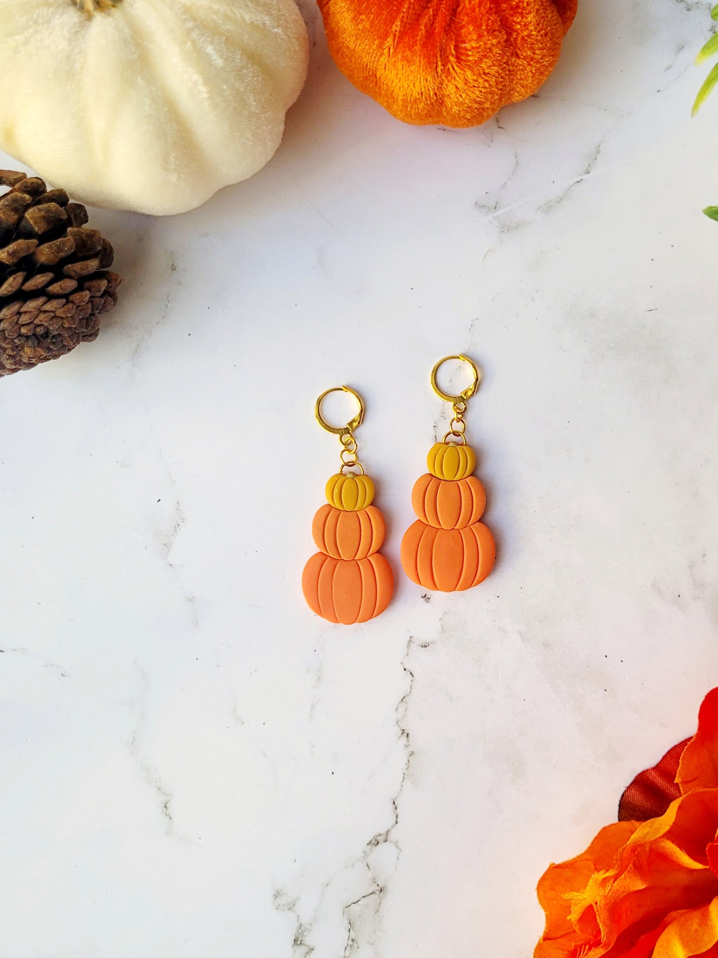Triple stack pumpkin earrings on a marble background with fall foliage. 